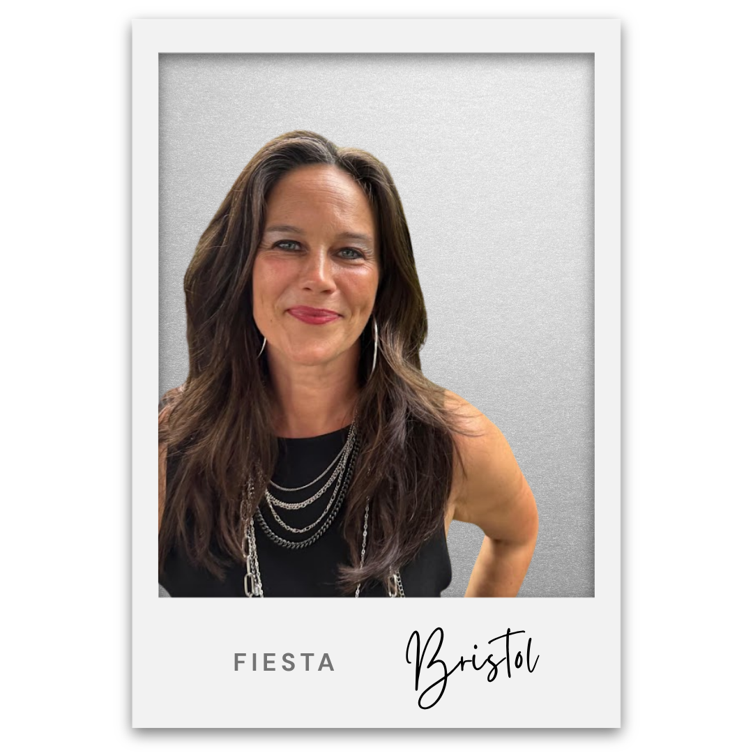 Mujer con cabello castaño oscuro y raya en la cara, sonriendo, vestida de negro con múltiples cadenas, en una foto tipo Polaroid con texto 'Fiesta Bristol'. Bristol Baughan