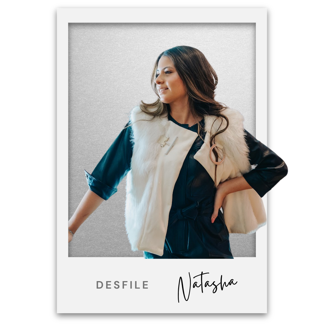 Mujer con cabello largo y ondulado, vestida con conjunto oscuro y chal de piel, posando sonriendo. Texto abajo dice 'Desfile Natasha'. Natasha Kindermann