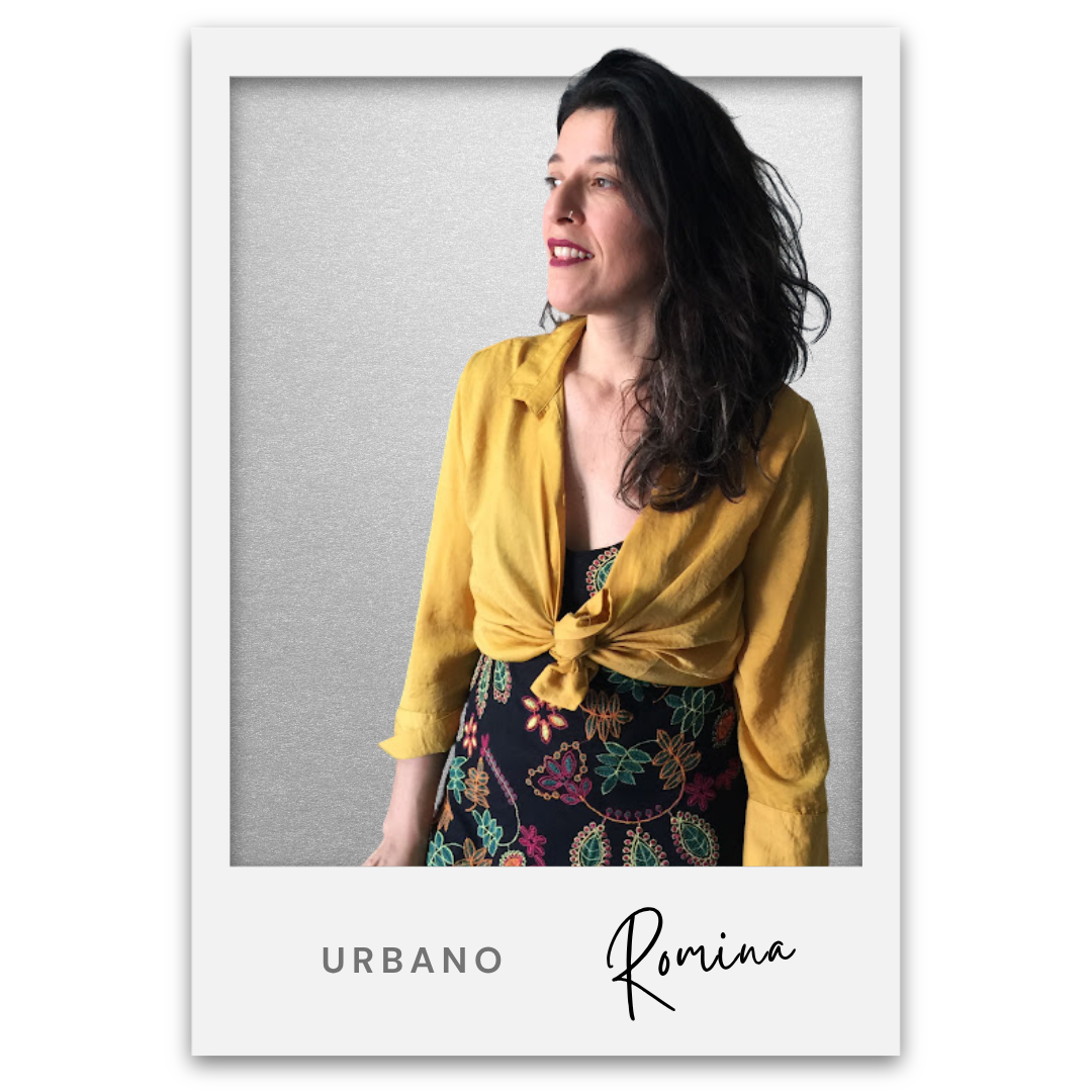 Mujer con blusa amarilla anudada en la cintura, falda con bordado de flores, pelo rizado y oscuro, sonriendo hacia la derecha, fondo gris. Romina Dias