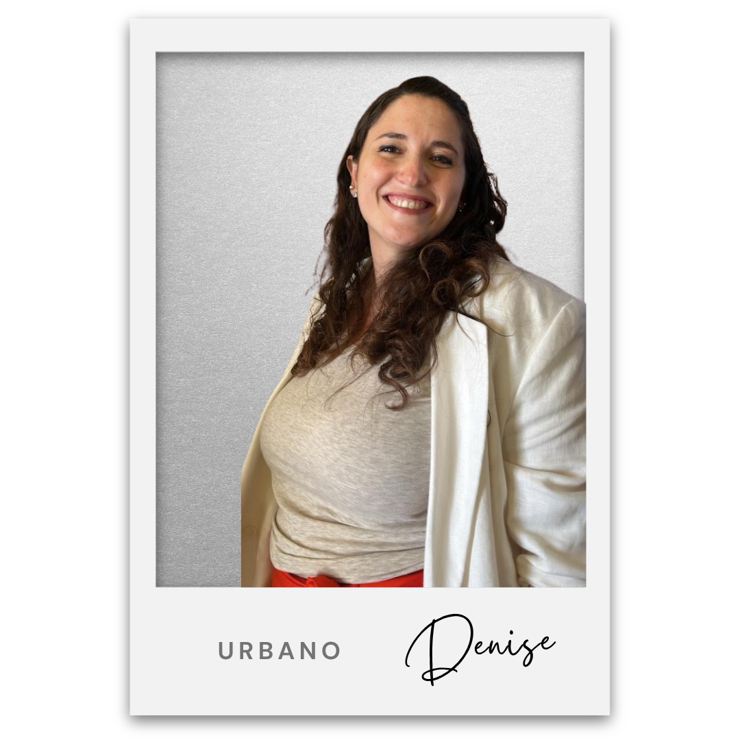 Una mujer sonriente con cabello rizado, camiseta beige, chaqueta blanca y pantalones rojos, posando frente a un fondo gris. Texto en la parte inferior dice 'Urbano Denise'. Denise Reyna Berrotaran