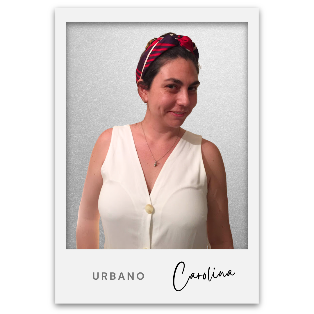 Retrato de una mujer sonriendo, lleva blusa blanca y una diadema roja y negra con rayas, fondo grisáceo, con texto que dice 'Urbano Carolina'. Carolina Li Gambi