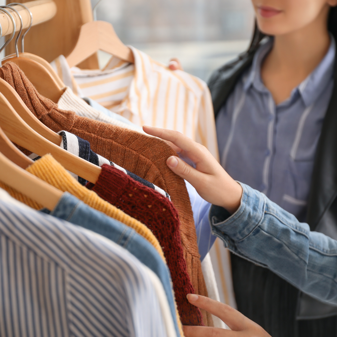 Personas mirando ropa en una tienda, sosteniendo y revisando varias prendas colgadas en perchas.