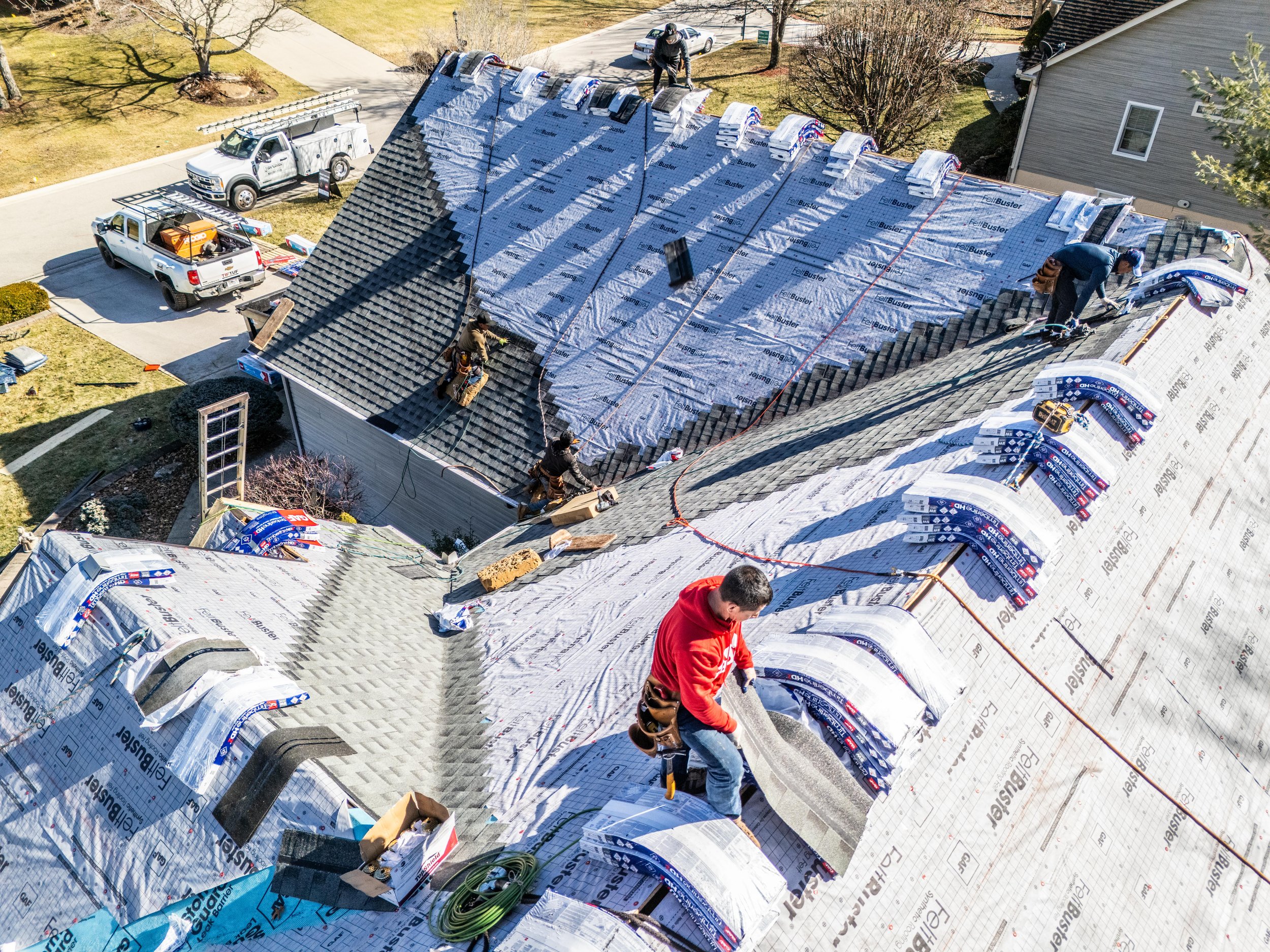 Roofers installing new shingles on a house in a residential area.