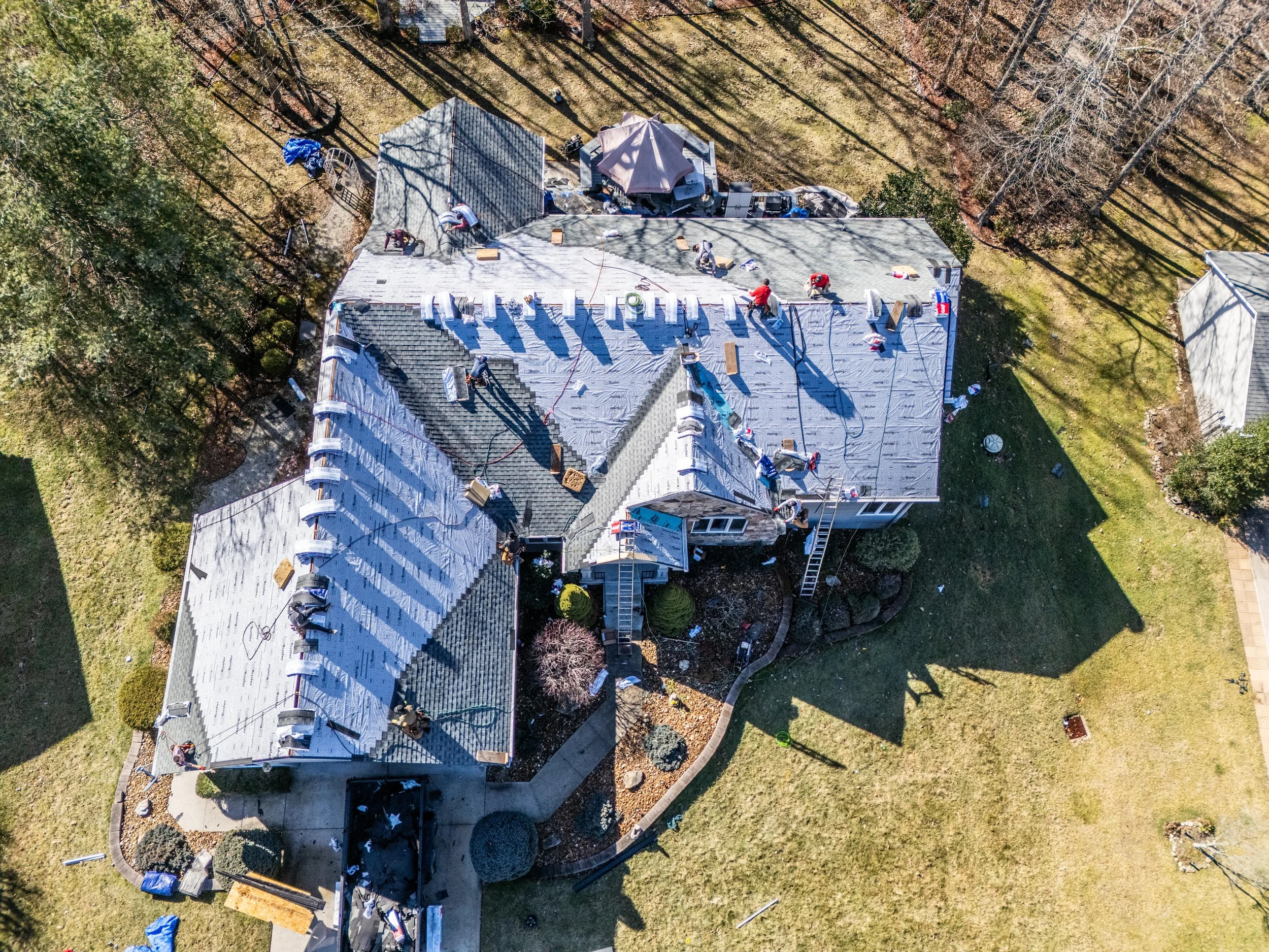 Aerial view of a house under roof renovation with workers and materials on the roof.