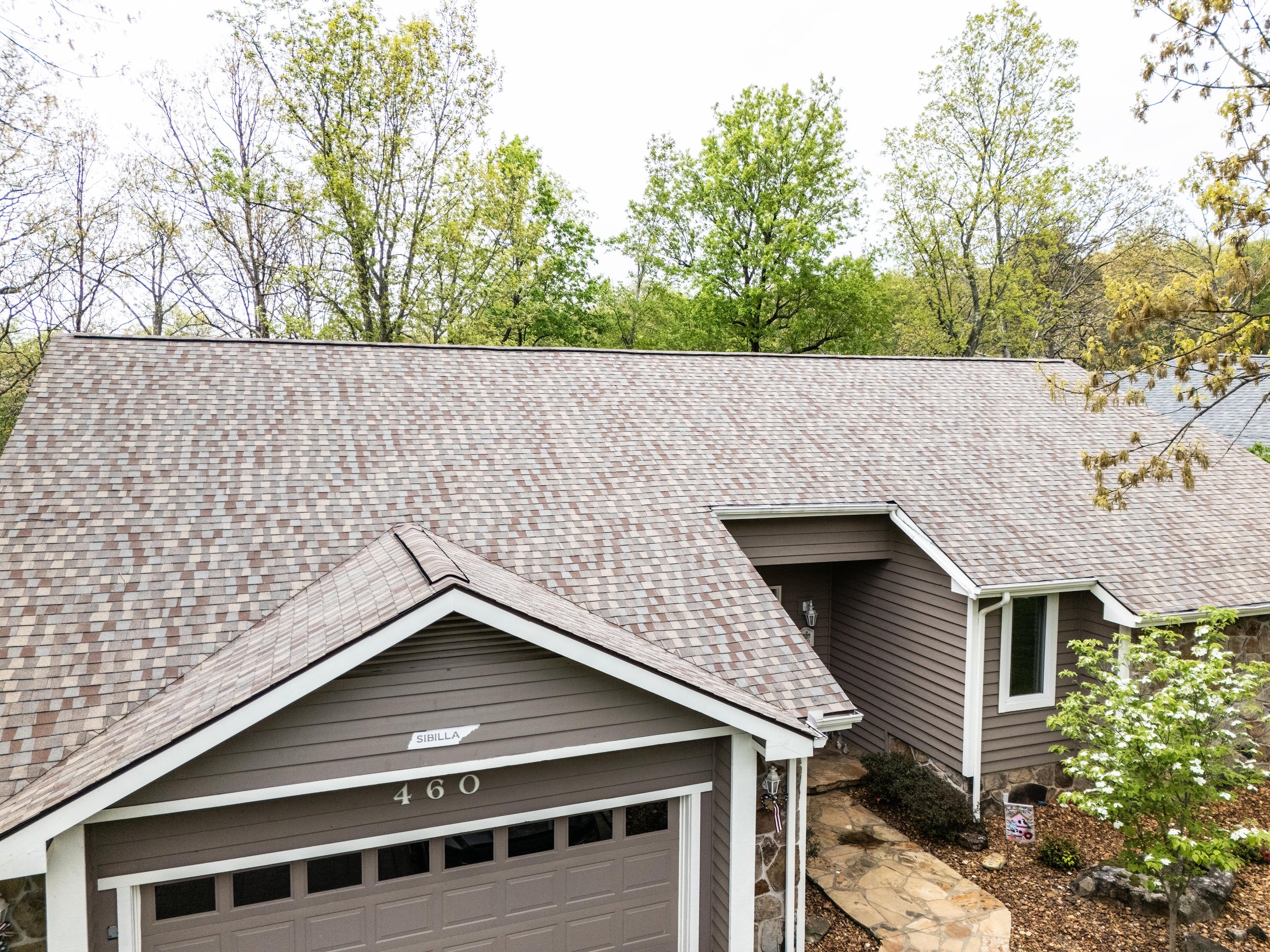 Residential house with brown roof and siding, surrounded by trees.
