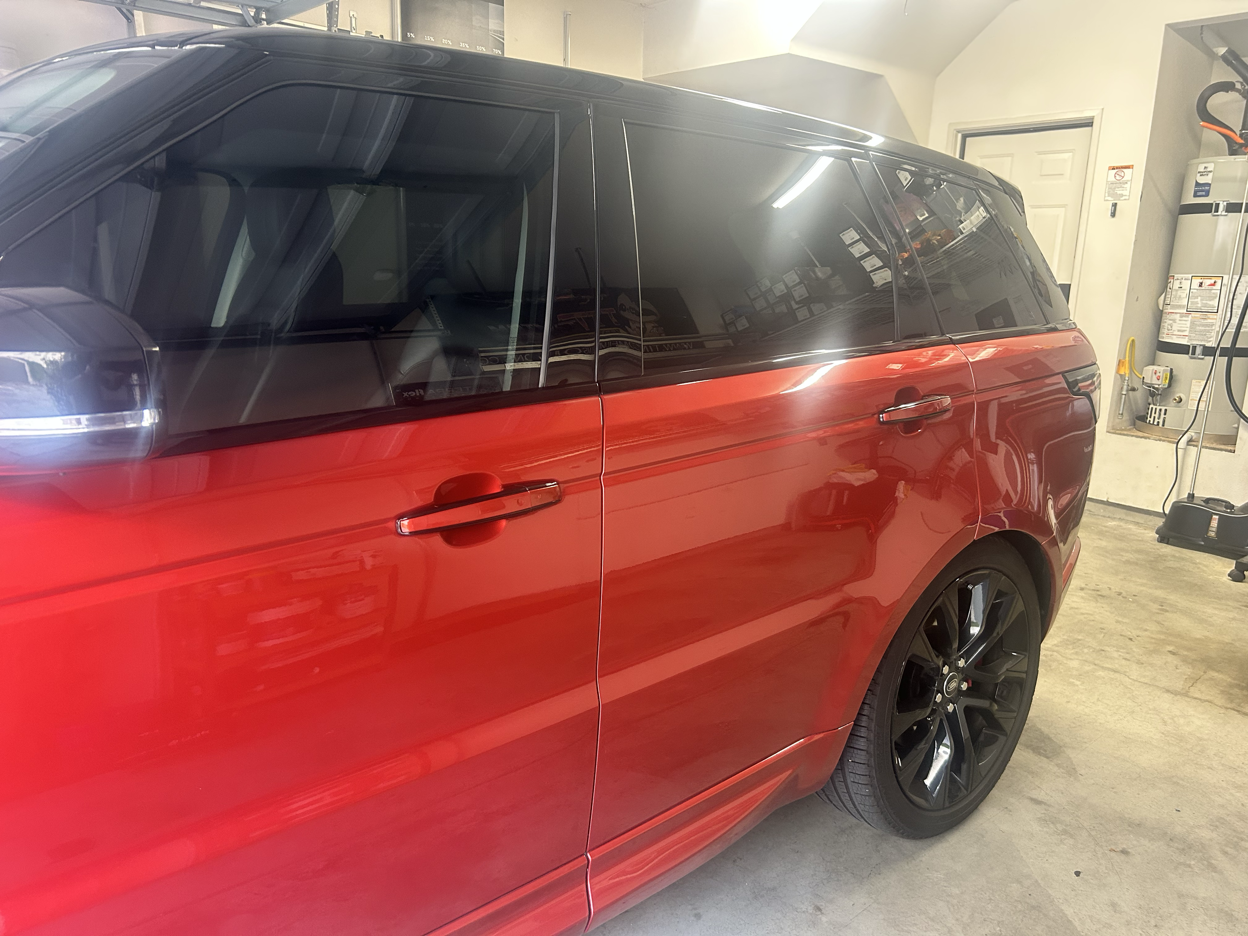 Red Range Rover SUV parked inside a garage with black wheels and tinted windows.