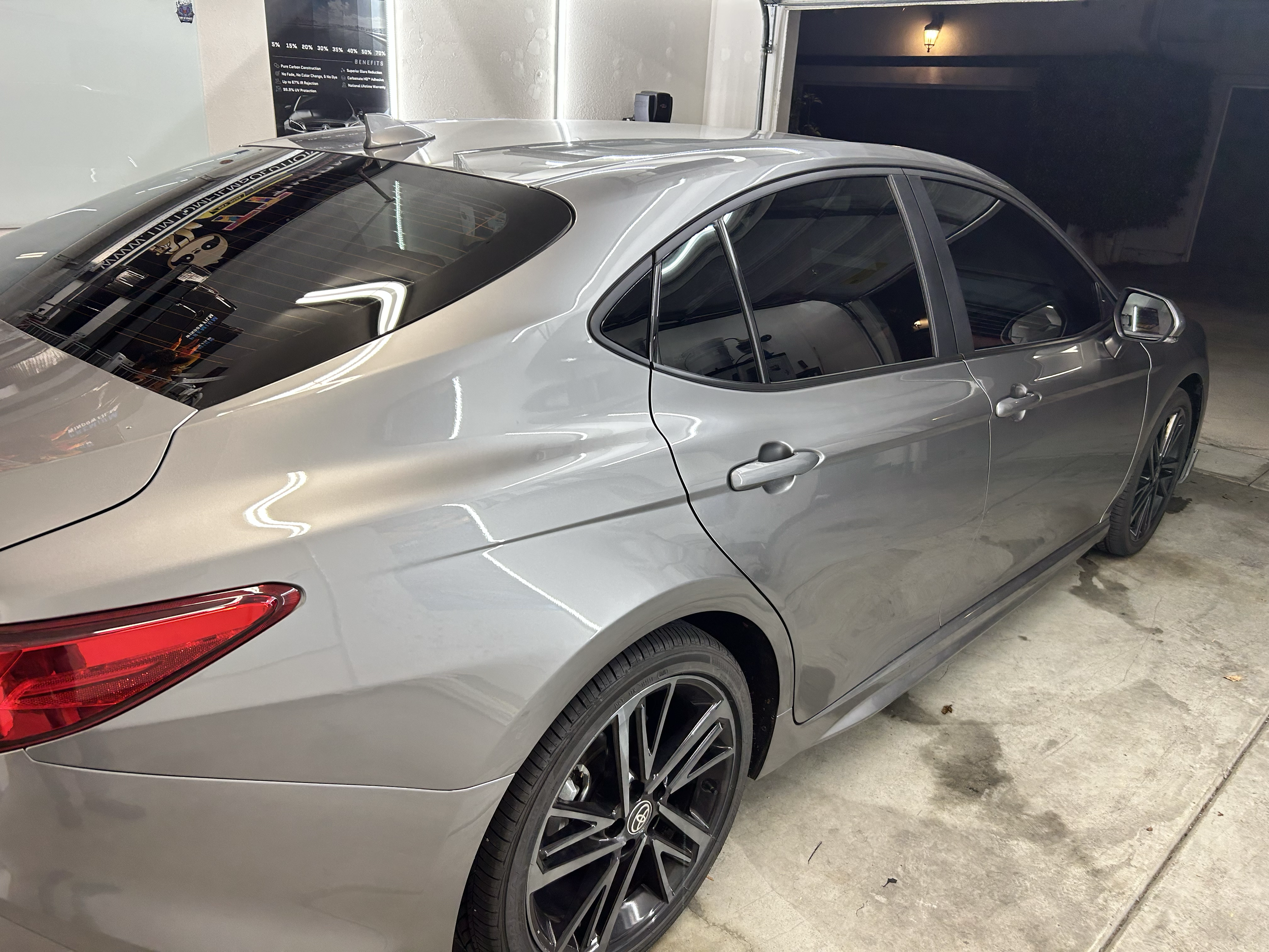 A silver sedan parked in a garage seen from the rear and side, with black wheels and tinted windows.