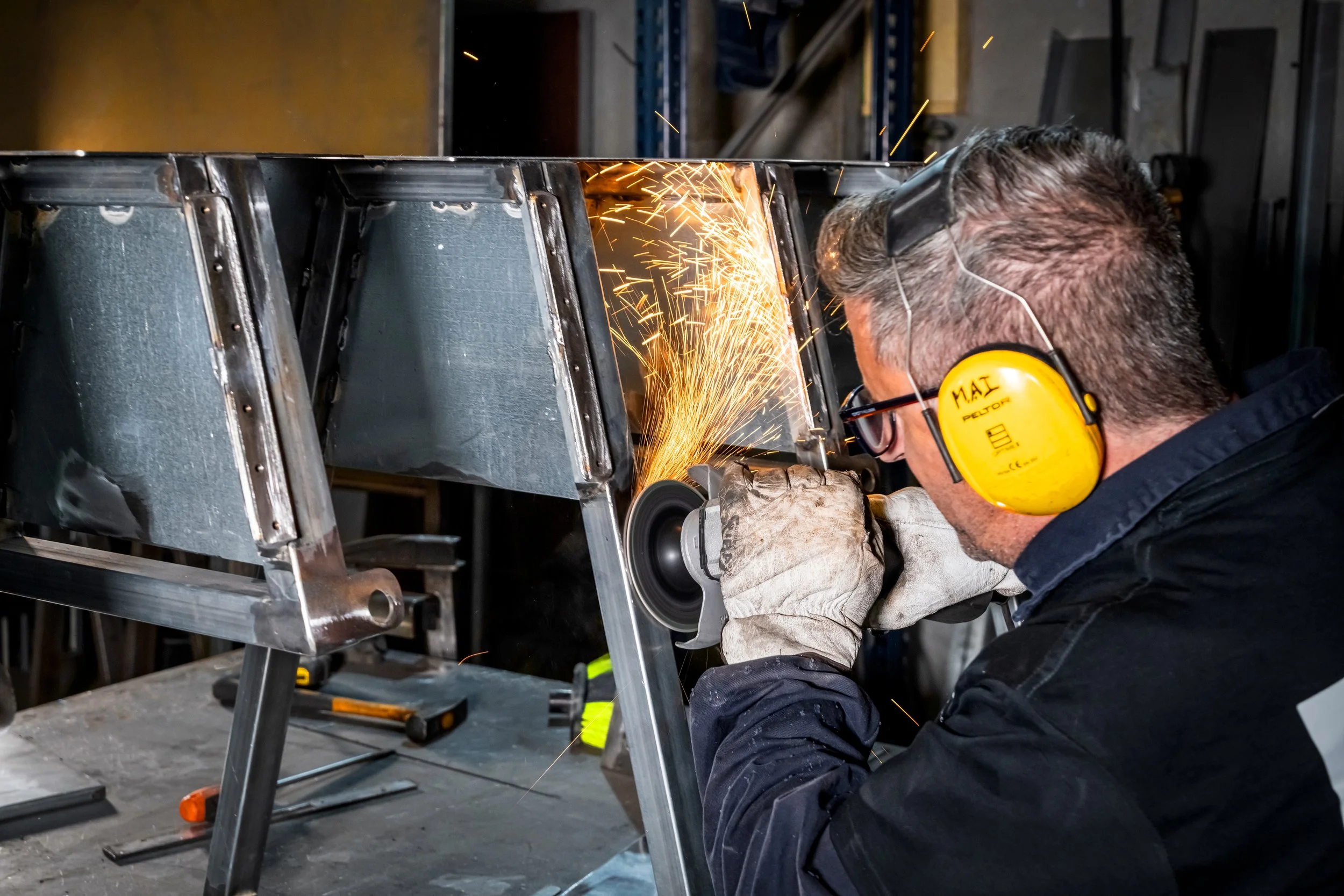 Un hombre trabajando con una amoladora en un marco metálico de Aparcapatinete, con chispas volando, en un taller mecánico