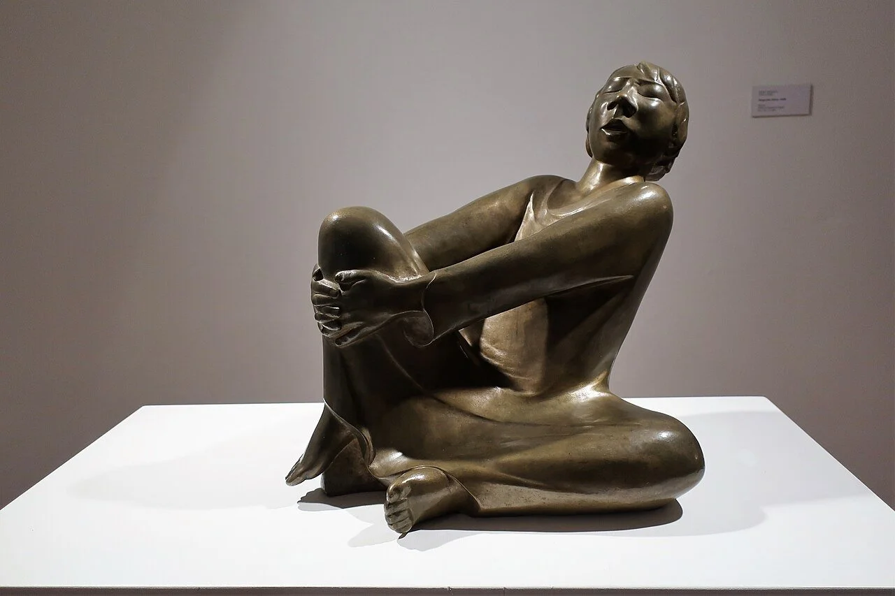 Bronze sculpture of seated man clasping his right knee and singing