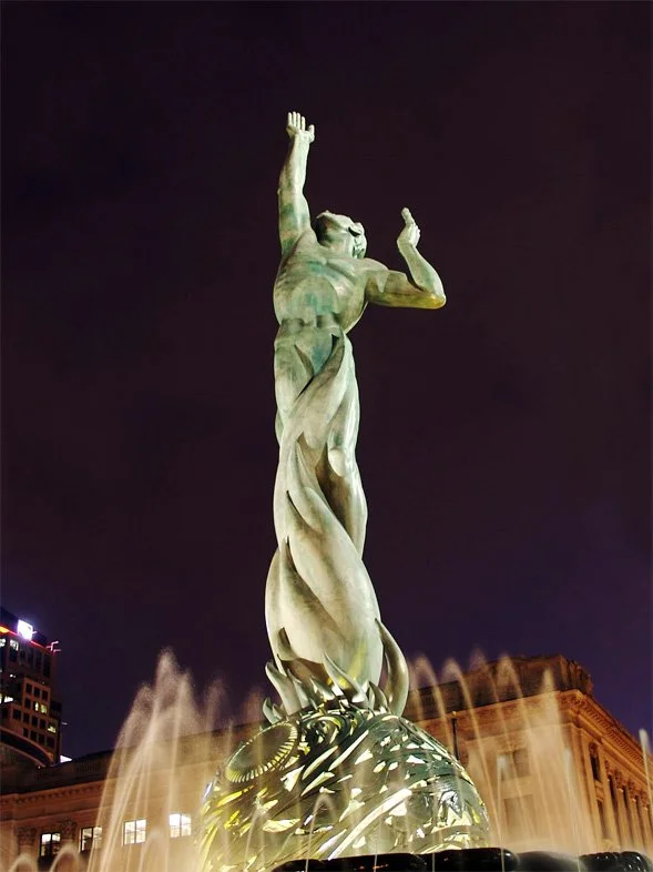 Sculpture of a human figure spiraling from below with arms and head lifted upward