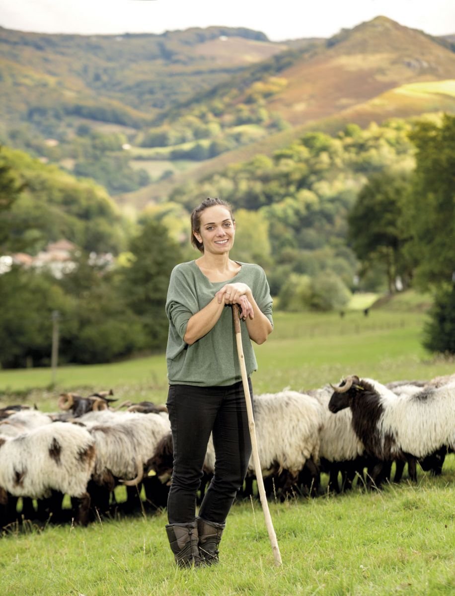 Smiling woman with shepherd’s staff and standing in front of sheep