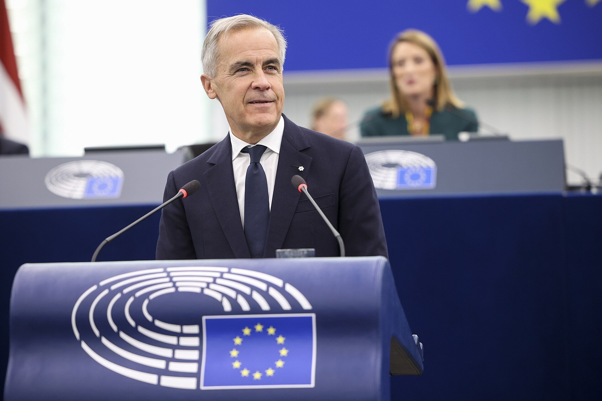 Smiling man in suit behind podium with a European Union flag