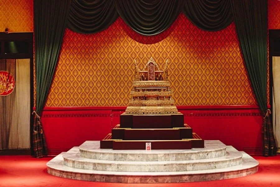Golden throne on a marble pedestal in a red room with a sign that says “Do not touch”