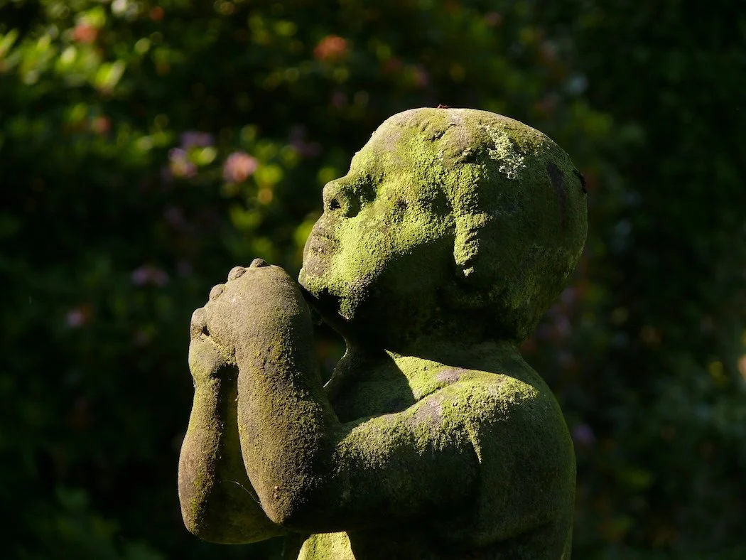 Moss-covered sculpture of a child praying