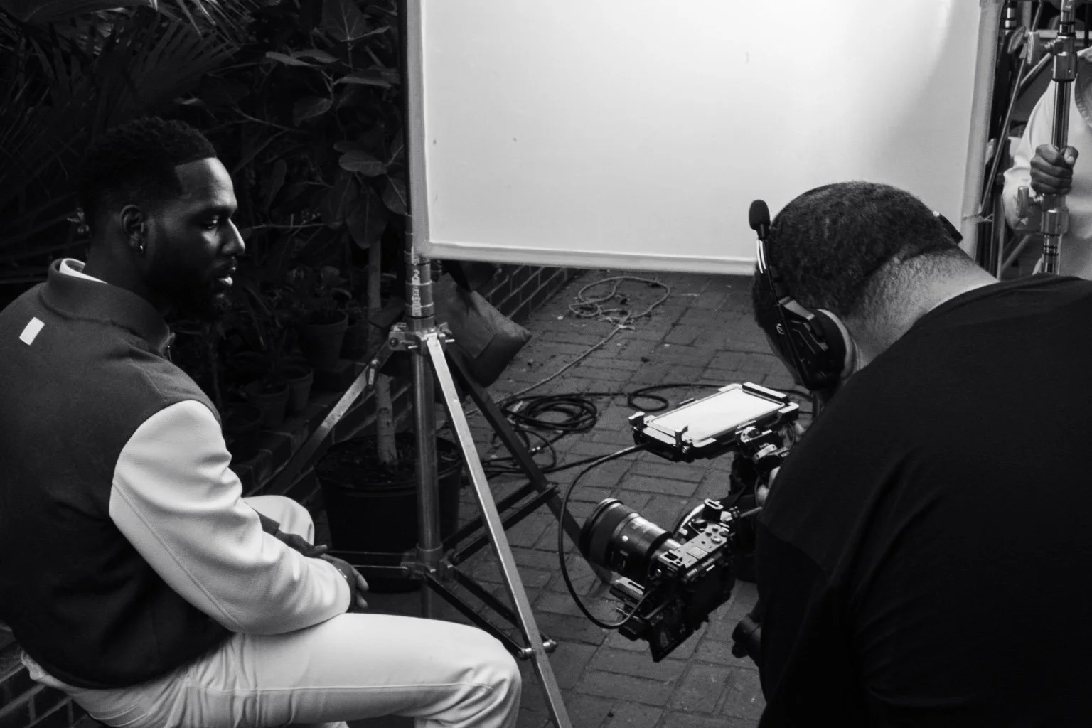 Kofi Siriboe seated while a camera operator frames a shot beside a diffusion screen during the ESSENCE shoot in New Orleans.