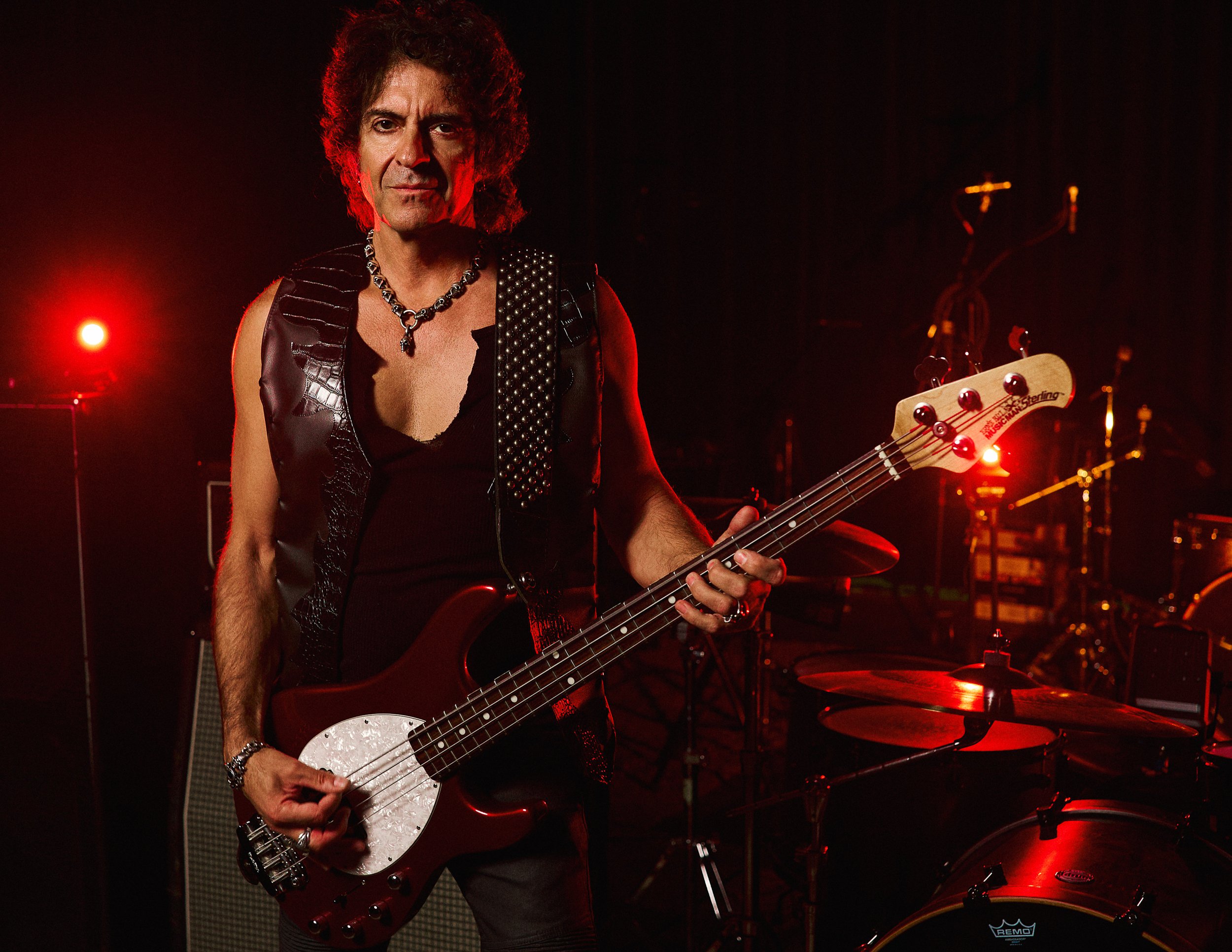 Portrait of Phil Soussan, bassist for Last In Line and Ozzy Osbourne collaborator, photographed holding his bass guitar in powerful red lighting.