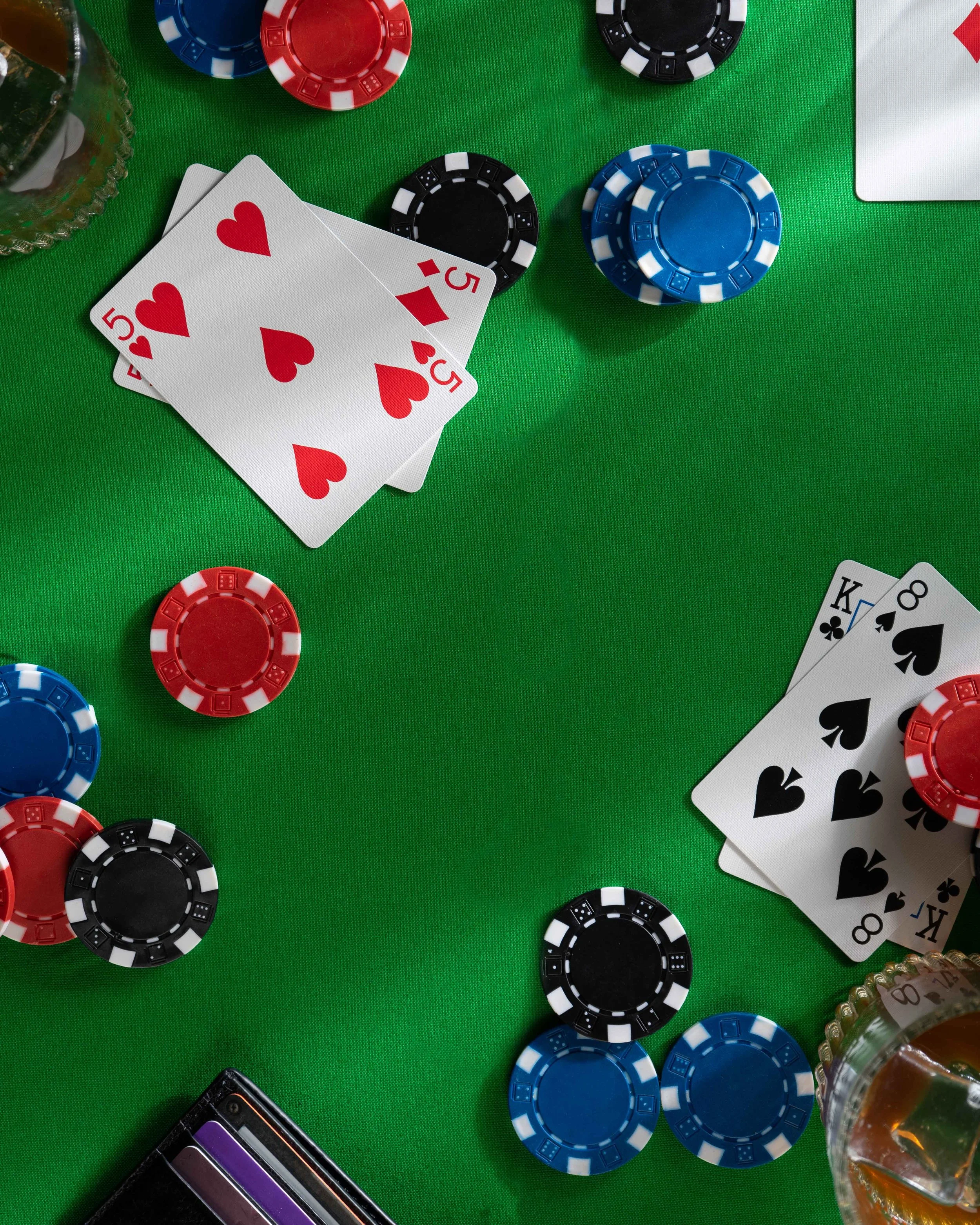 Poker chips, playing cards, and a glass of whiskey on a green table.