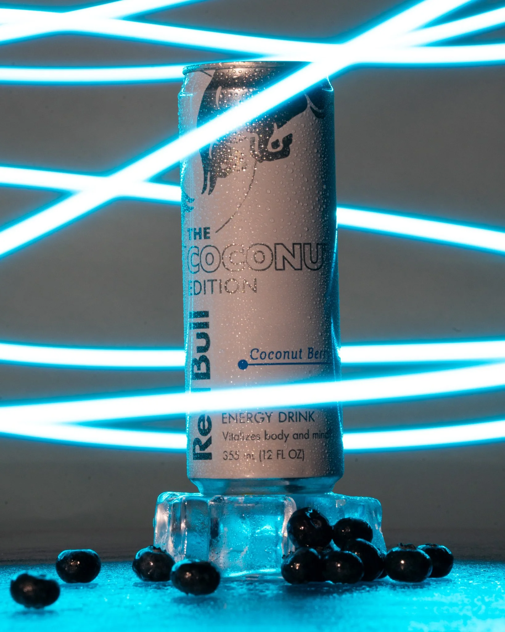 Canned Red Bull energy drink labeled 'Rebull The Coconut Edition' with blueberries and ice cubes at the base, illuminated by blue neon light streaks.
