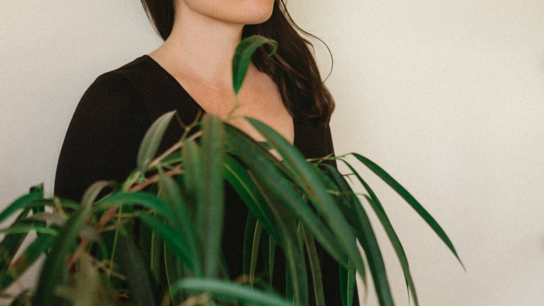 Woman's torso wearing black shirt with green plant in front