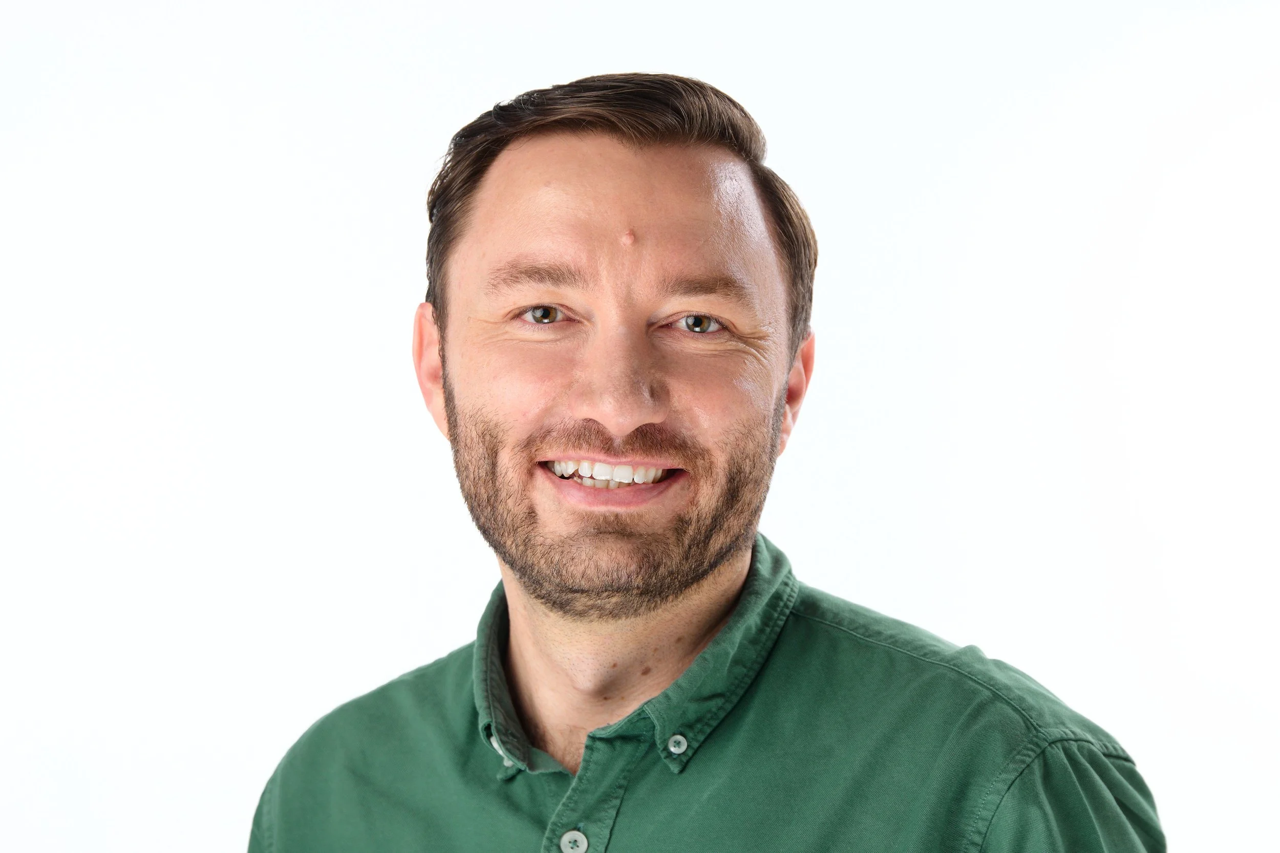 A smiling man with short brown hair and a beard, wearing a green button-up shirt, against a white background.