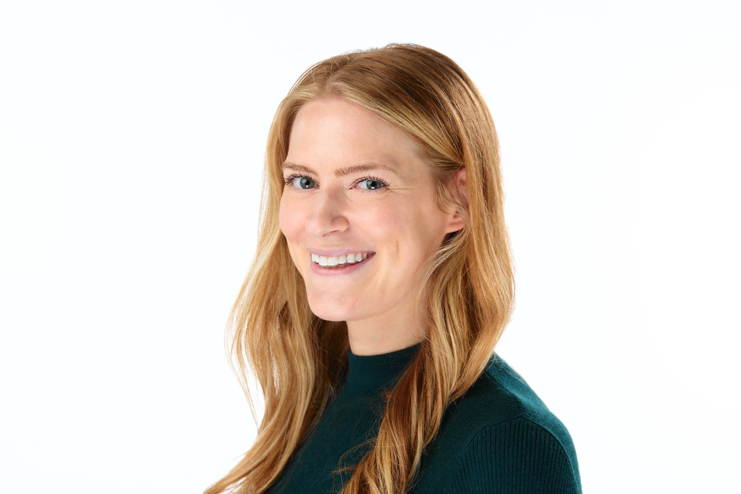 Portrait of a red-haired woman smiling, wearing a dark green sweater, against a white background.