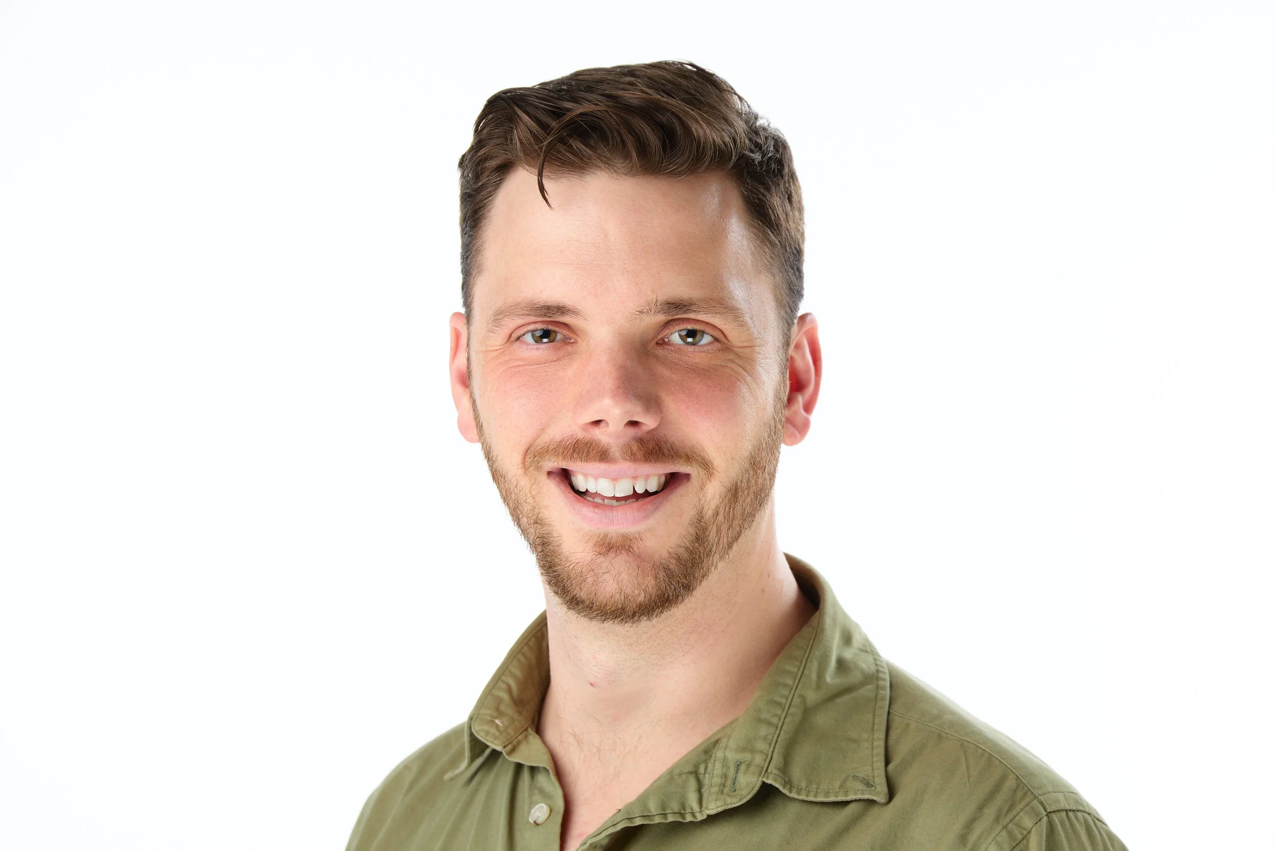 A smiling young man with short brown hair and a beard, wearing an olive green shirt, against a plain white background.