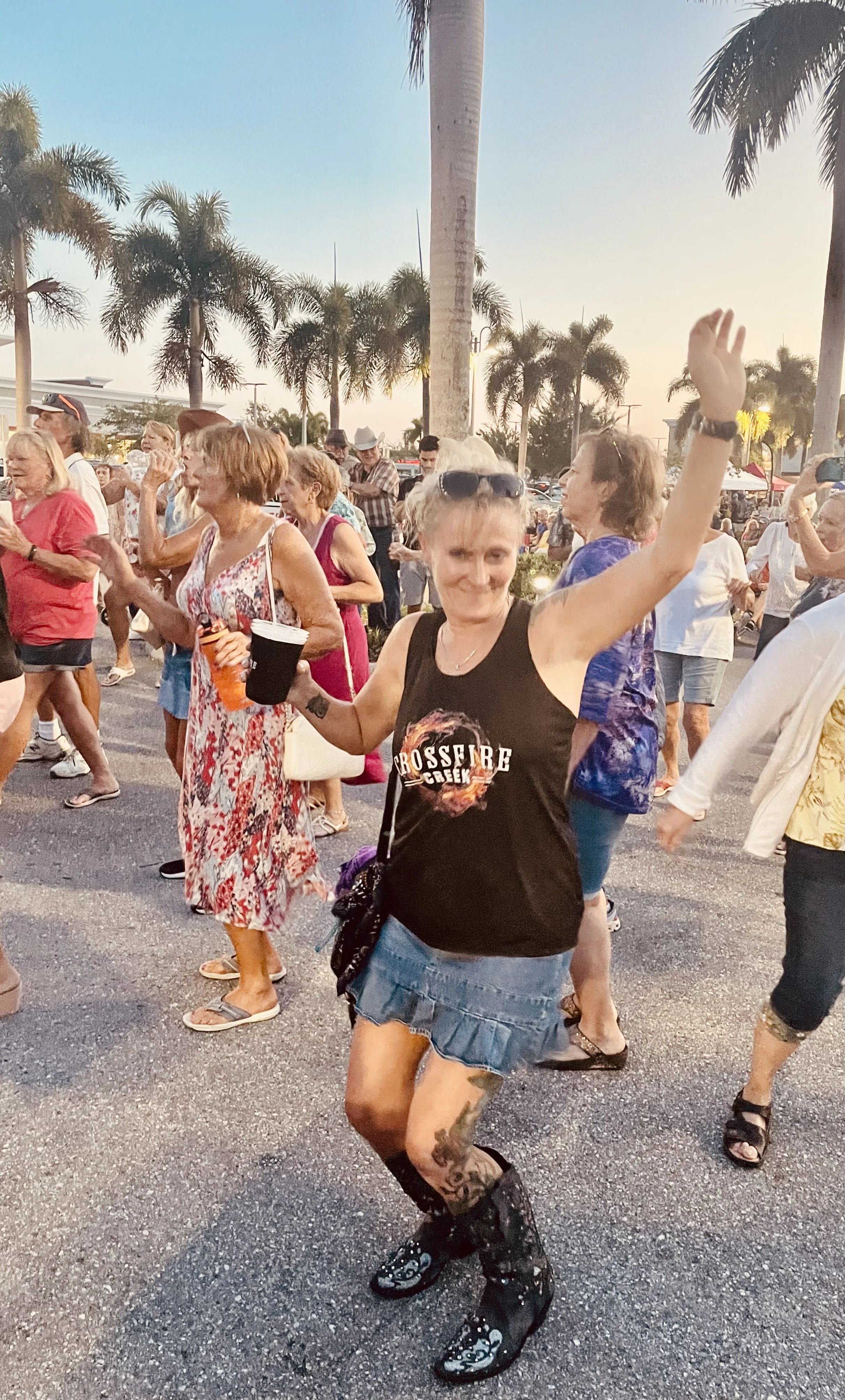 People dancing at an outdoor event with palm trees in the background.