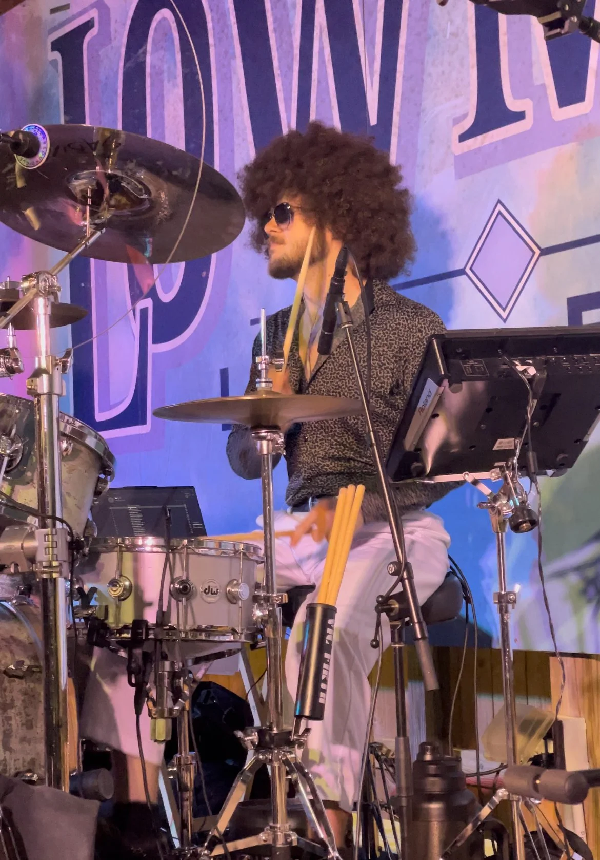 Man with afro and sunglasses playing drums at a live performance.