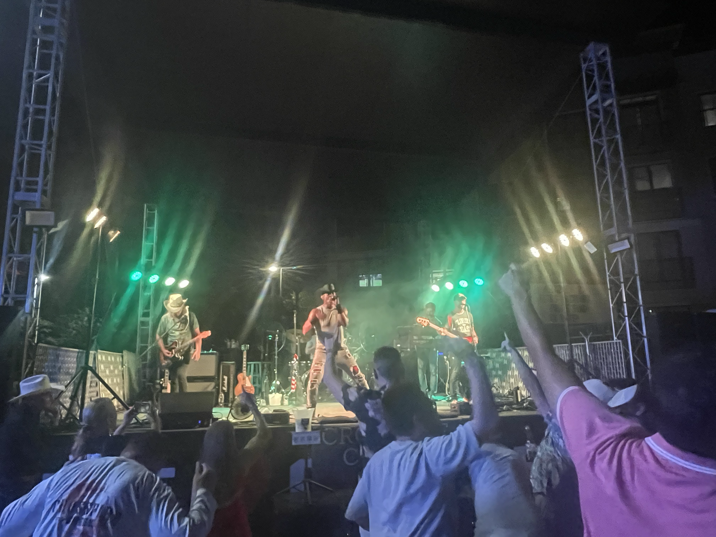 Live country music band performing on an outdoor stage at night with colorful stage lights and a cheering audience.