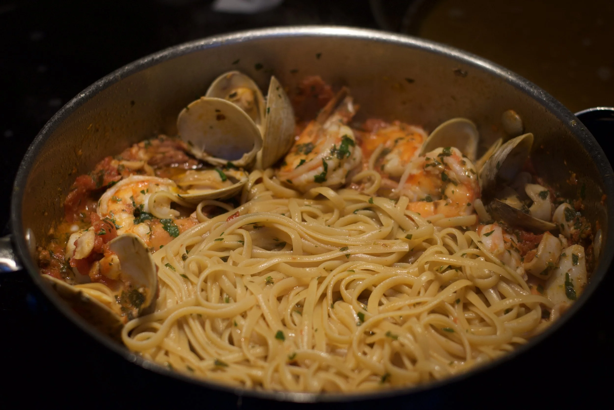 A pot of cooked spaghetti pasta with seafood, including clams and shrimp, in a tomato sauce with herbs. Pescatore