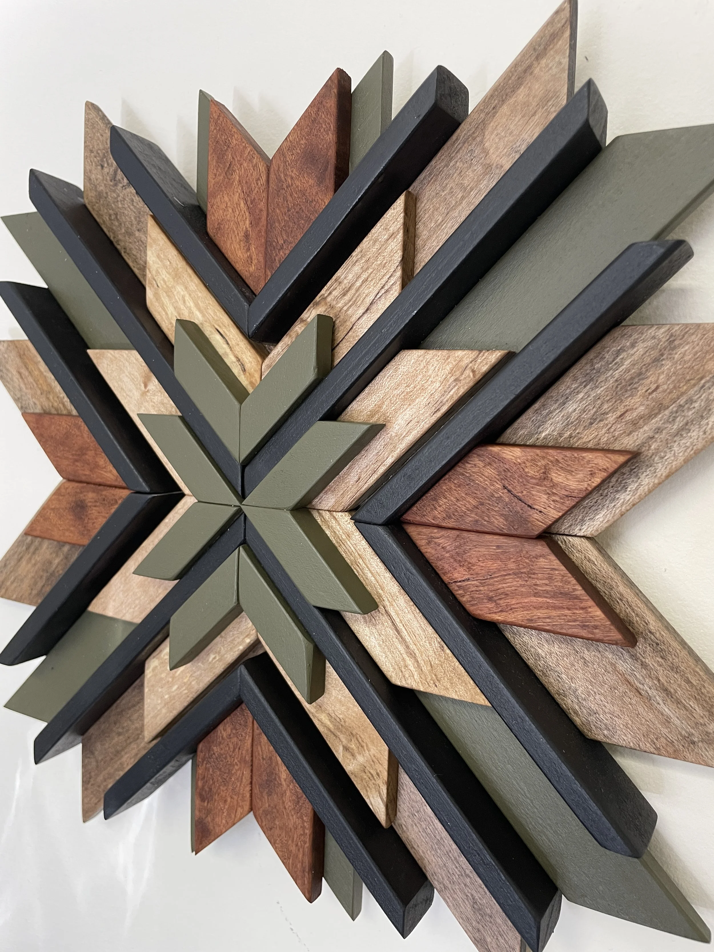 Close up view of a handcrafted wooden sunburst mosaic in black and green paints with natural and espresso stains.