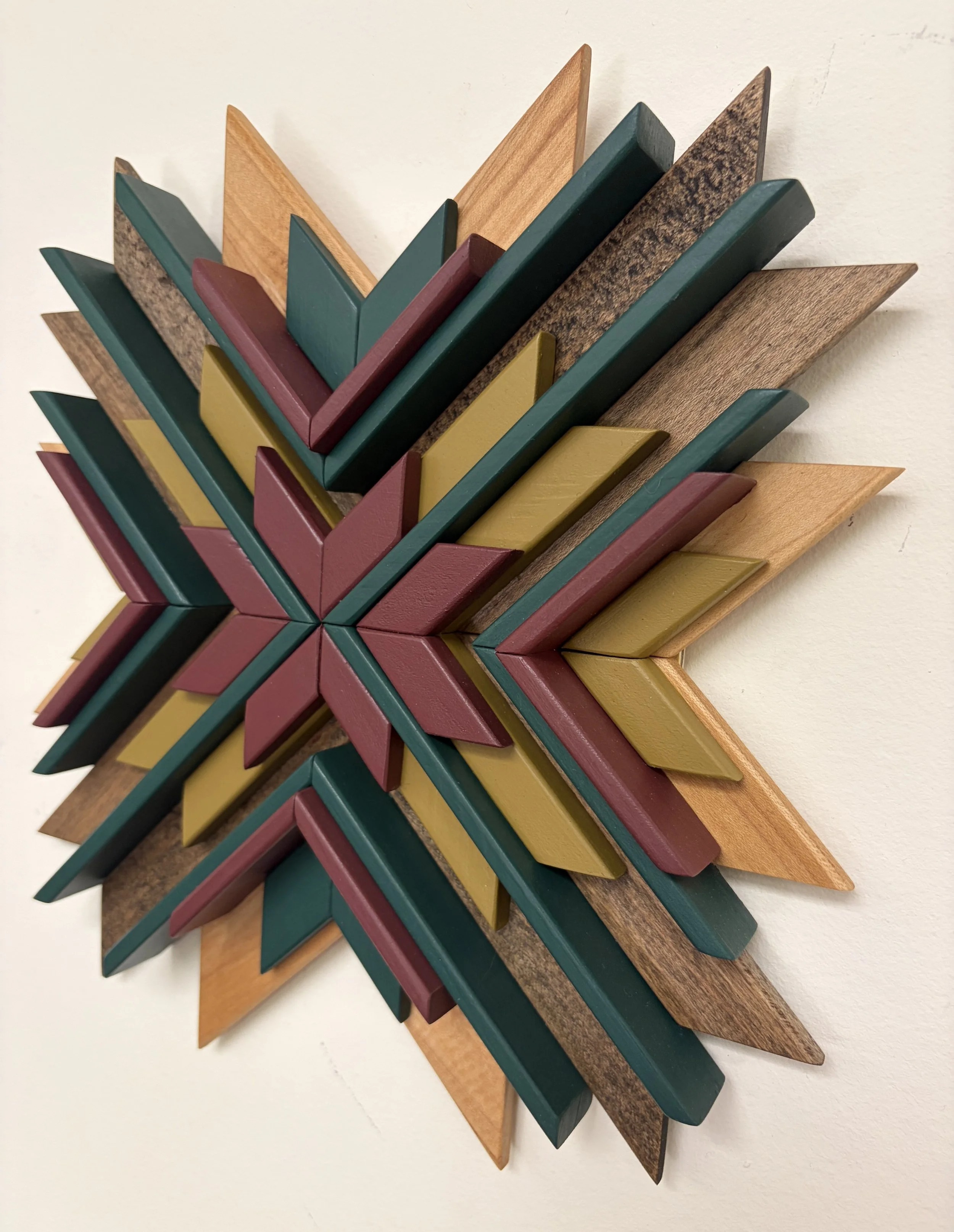 Angled view of a sunburst style wooden mosaic in pink, teal, and bright green paint with natural and espresso stains.