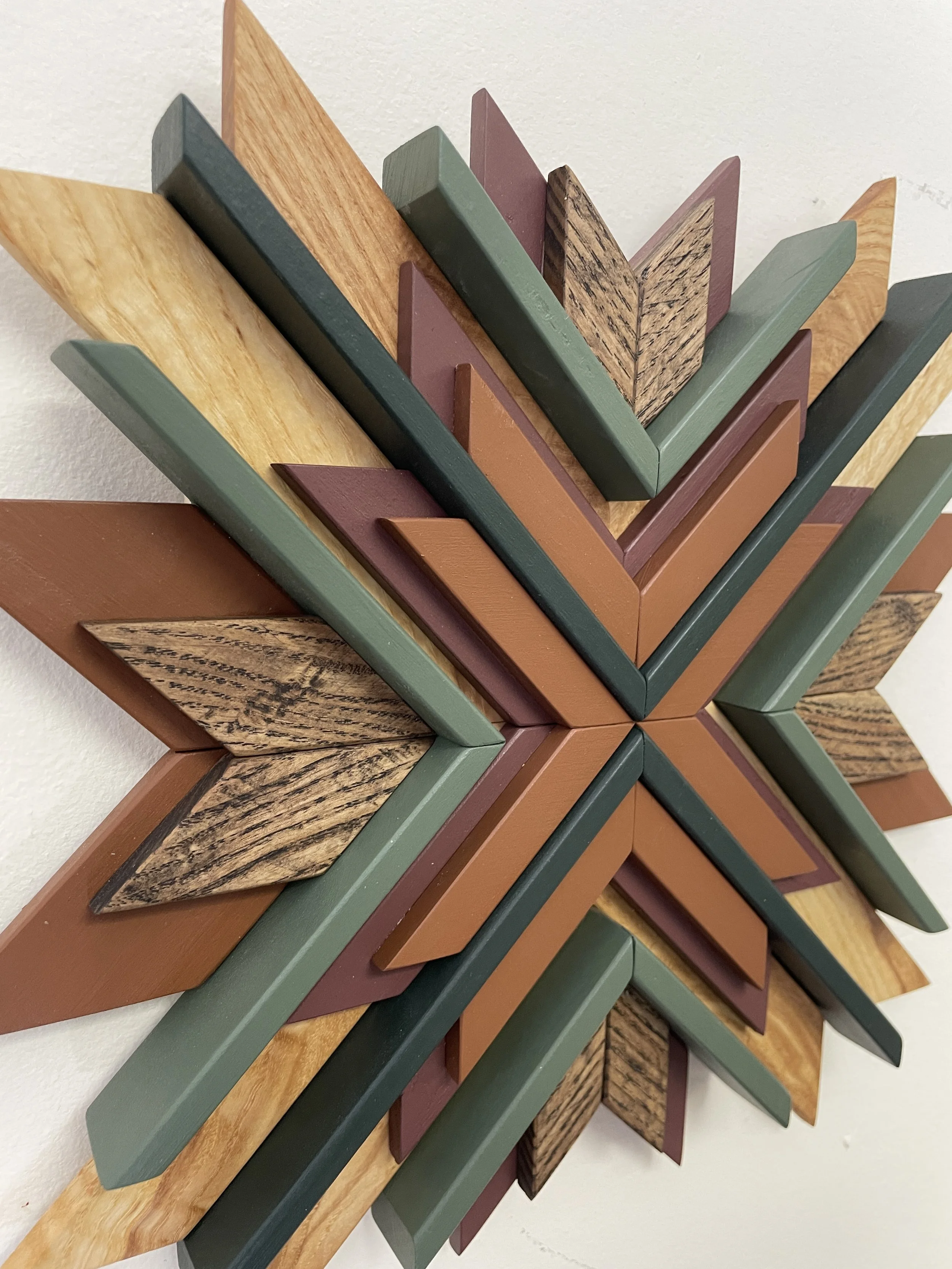 Side view of a handcrafted sunburst style wooden mosaic in pink, orange, and two  different green paints with natural and espresso stains.