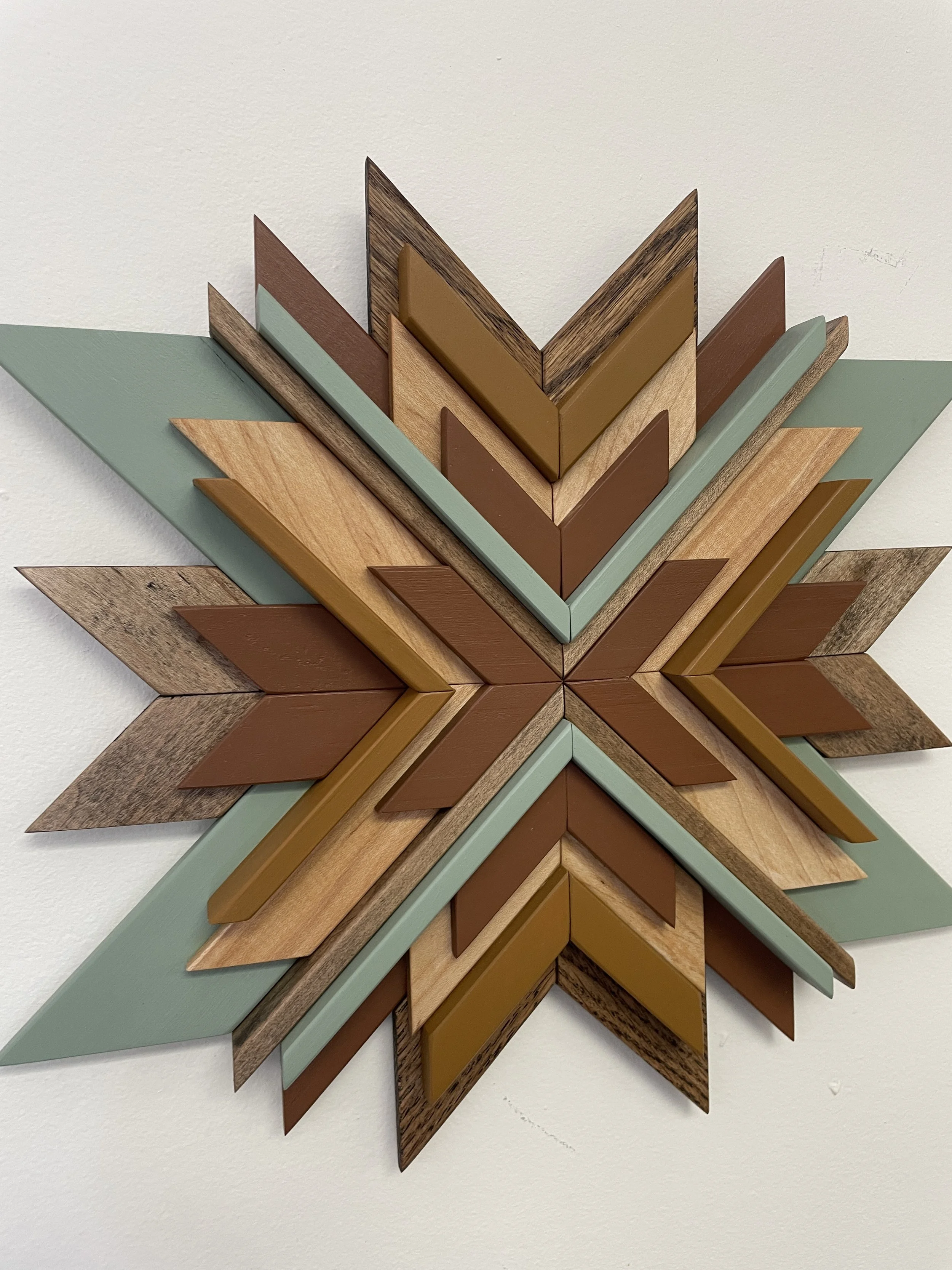 Angled view of a handcrafted wooden sunburst mosaic in green, yellow, and orange paints with natural and espresso stains.