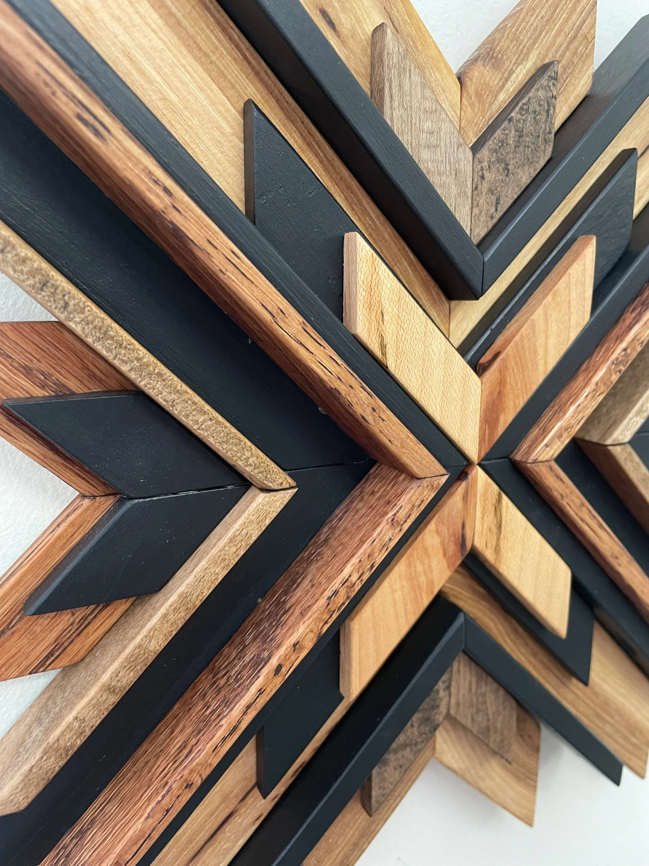 Detailed view of a handcrafted sunburst style wooden mosaic in black paint with natural, espresso, and red mahogany stains.