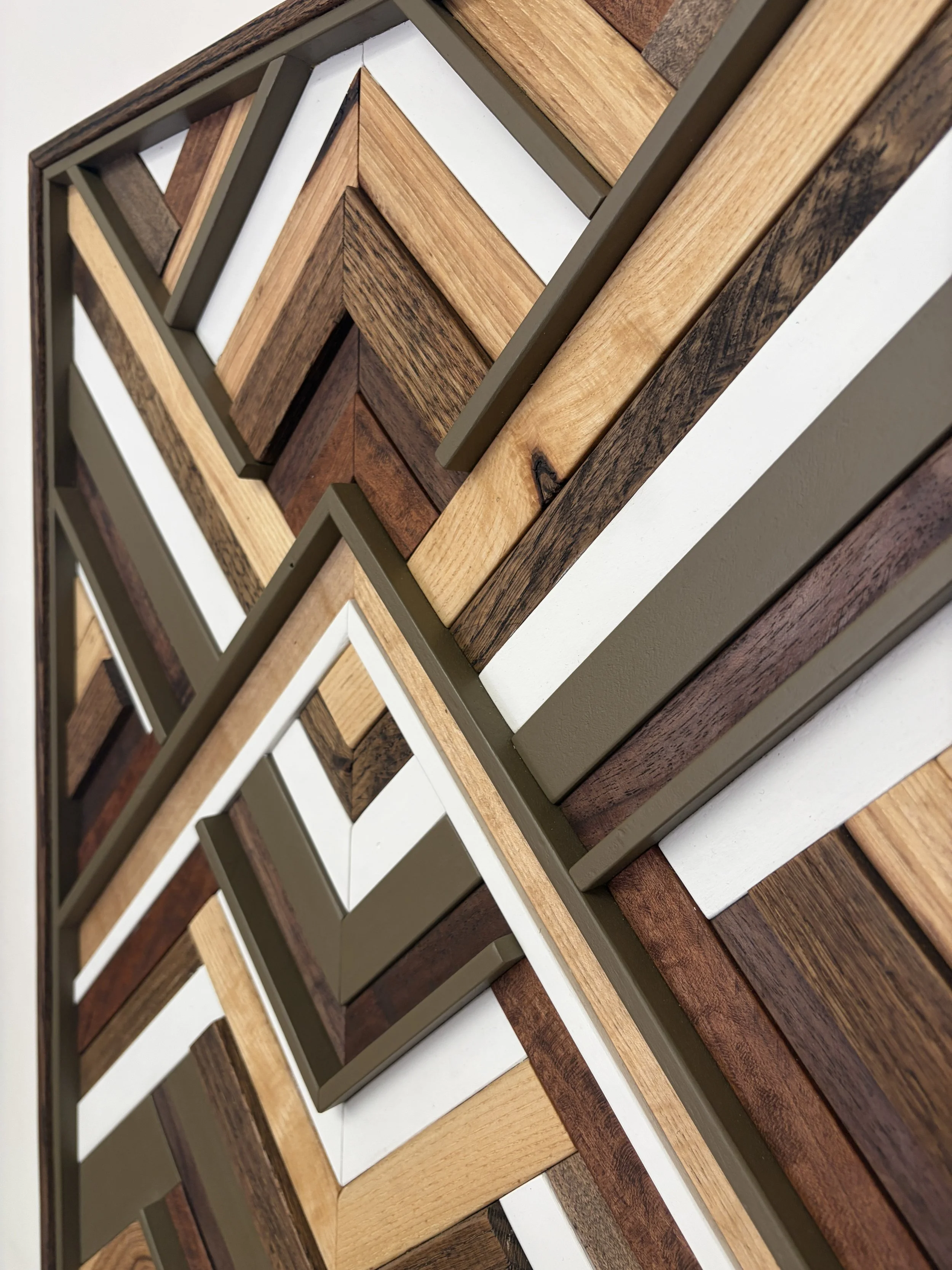 Zoomed in side view of a handcrafted framed wooden mosaic in white and light olive green paint with natural, espresso, and red mahogany stains.