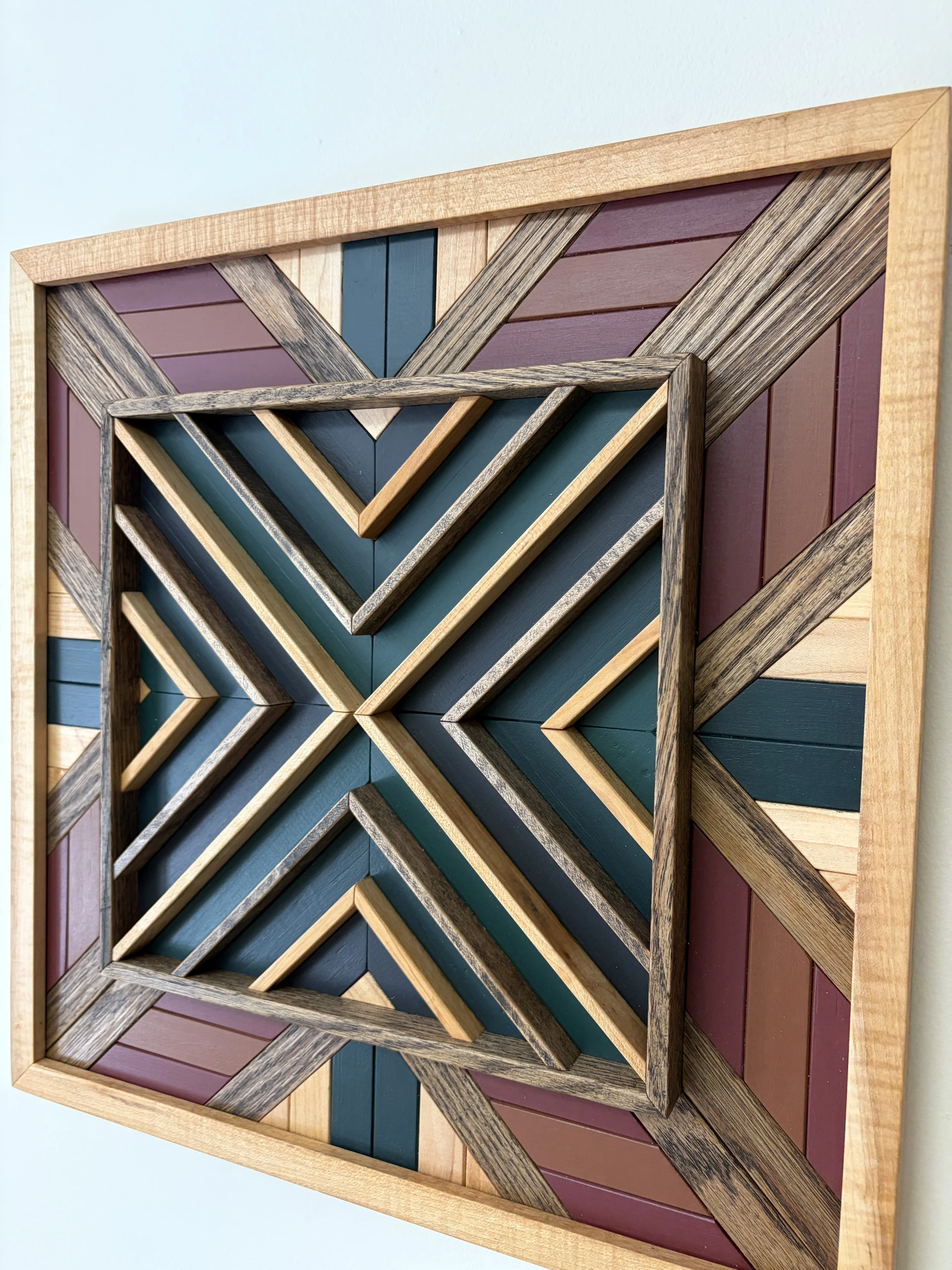 Angled view of a handcrafted framed wooden mosaic in black, green, teal, pink, and orange paint with natural and espresso stains.