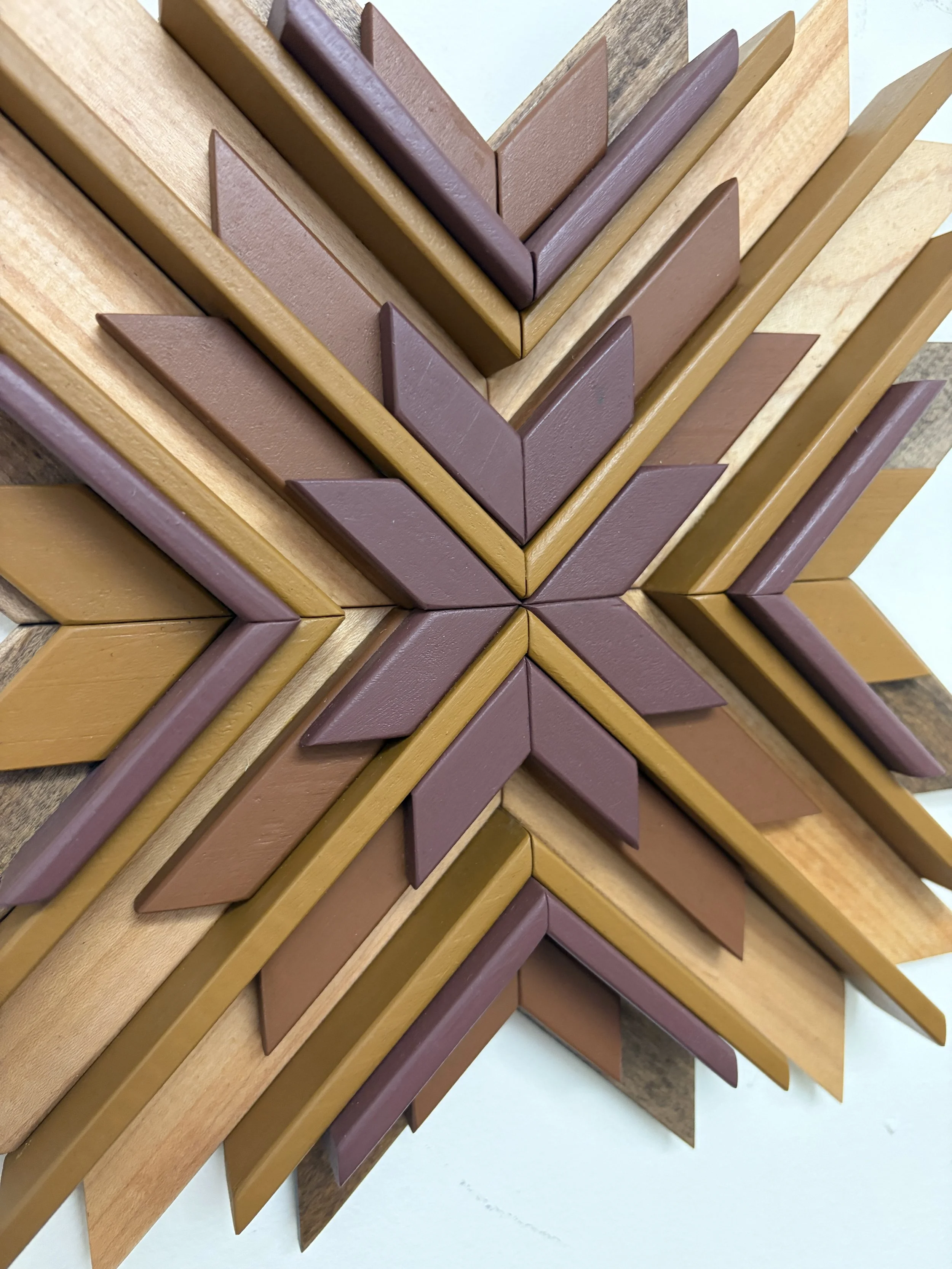 Close up view of a wooden sunburst style mosaic in pink, orange, and yellow paint with natural and espresso wood stains.