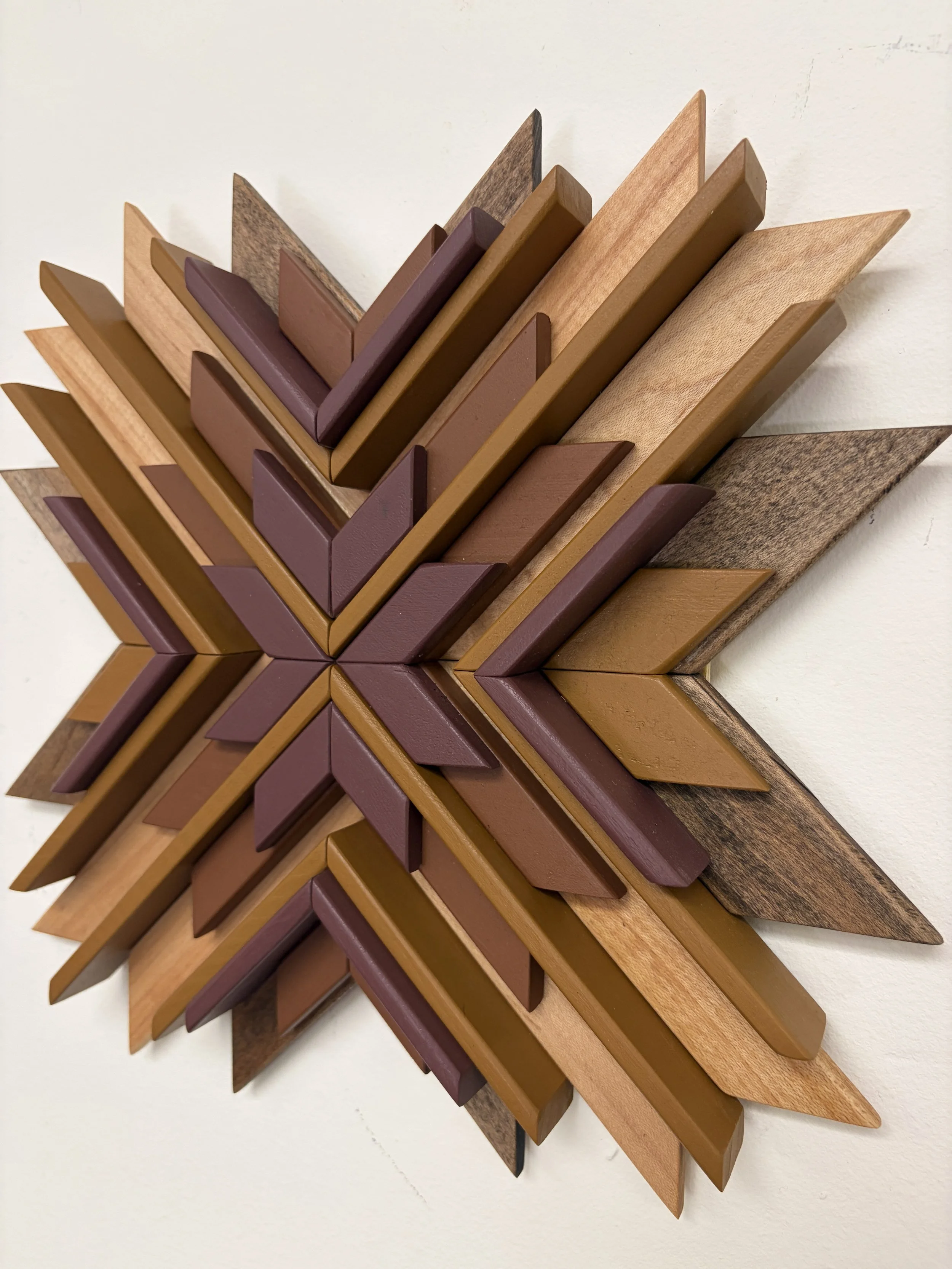 Angled view of a wooden sunburst style mosaic in pink, orange, and yellow paint with natural and espresso wood stains.