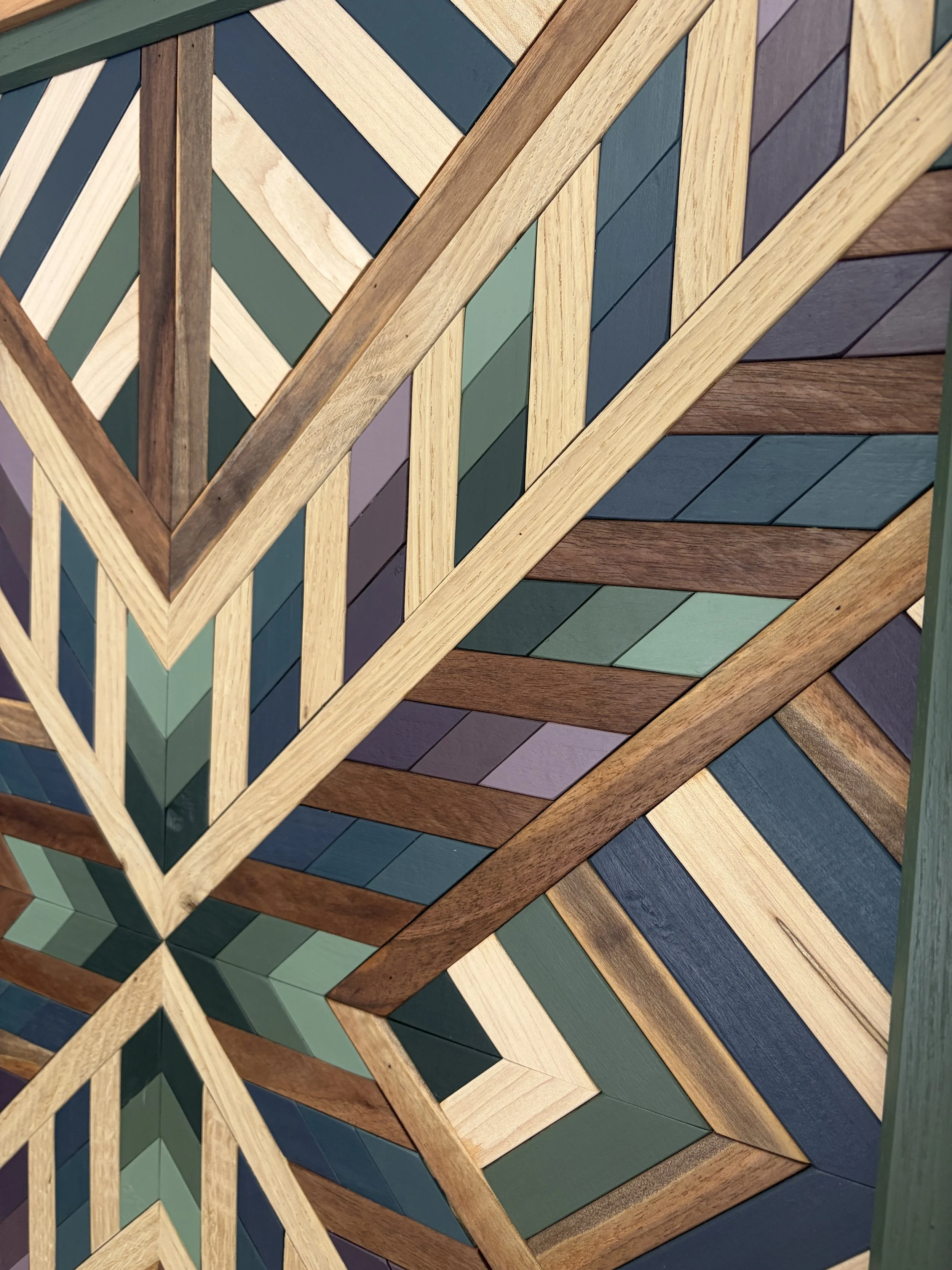 Close up view of a framed wooden mosaic in several shades of blue, green, and purple paint with natural stains.
