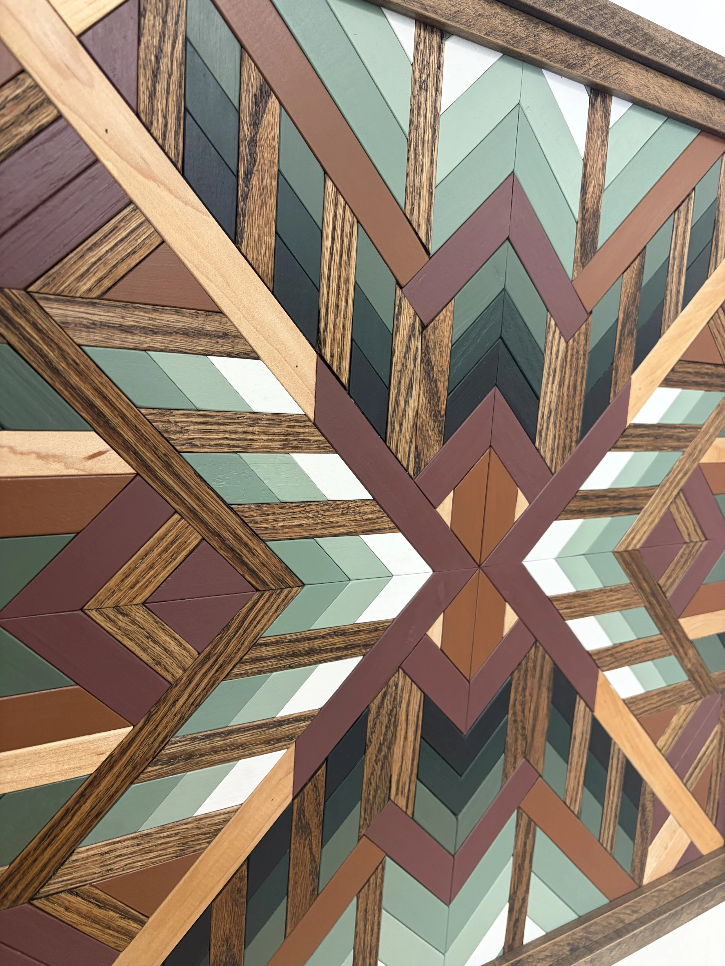 Close up view of a handcrafted framed wooden mosaic in black, white, pink, orange, and various green paints with natural and espresso stains.