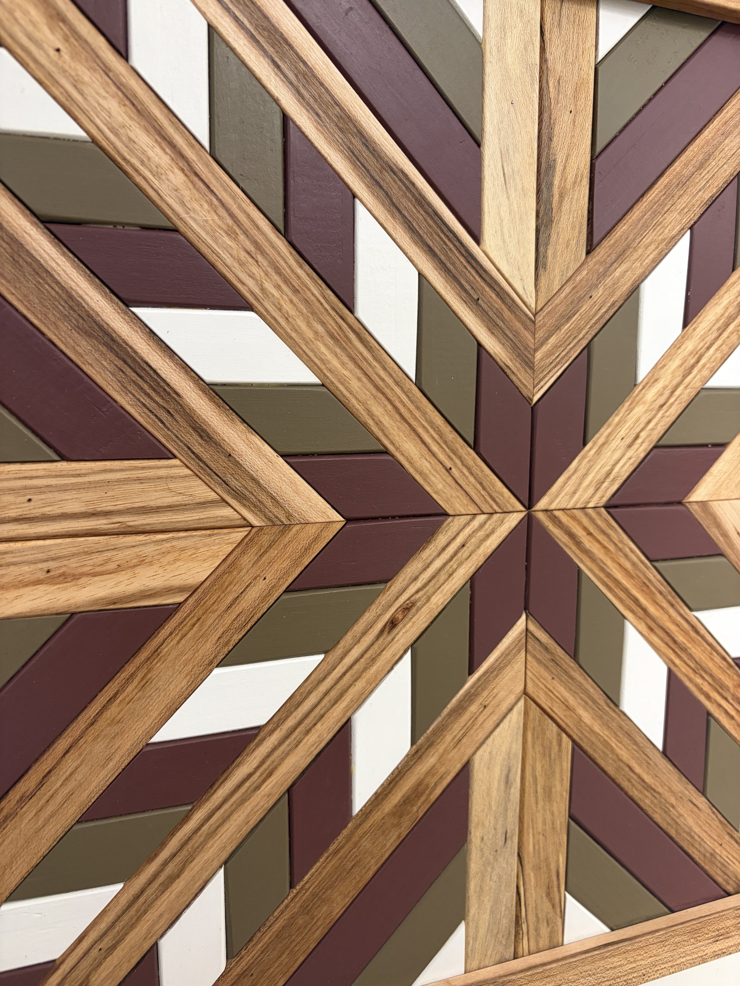 Close up view of a handcrafted framed wooden mosaic in white, pink, and green paint with natural stains.