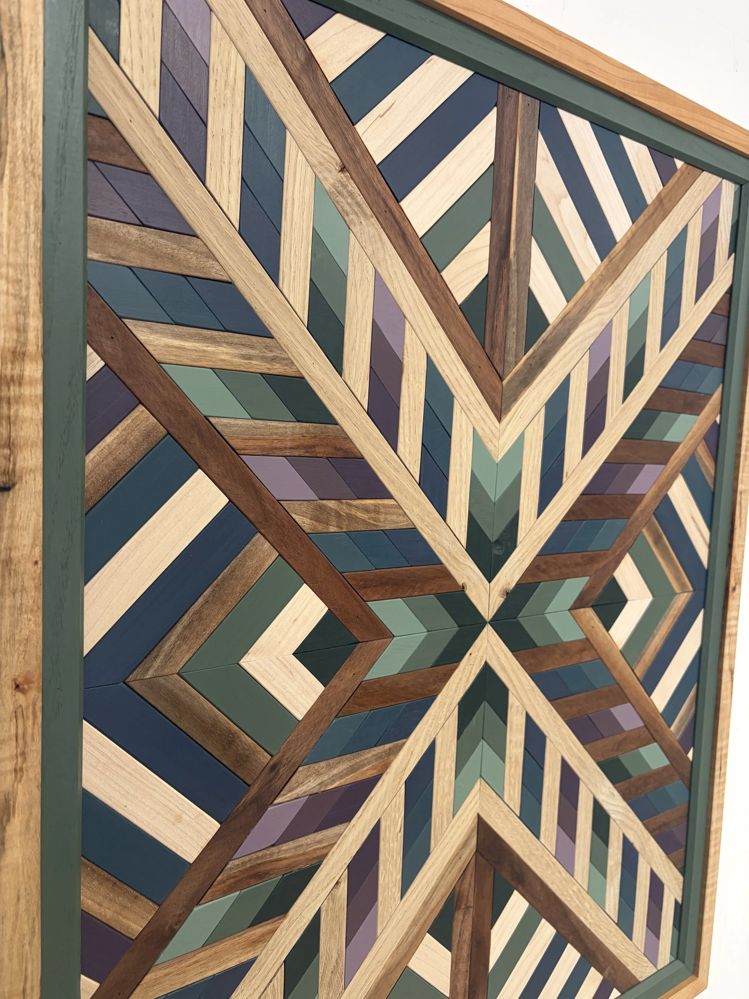 Side view of a framed wooden mosaic in several shades of blue, green, and purple paint with natural stains.