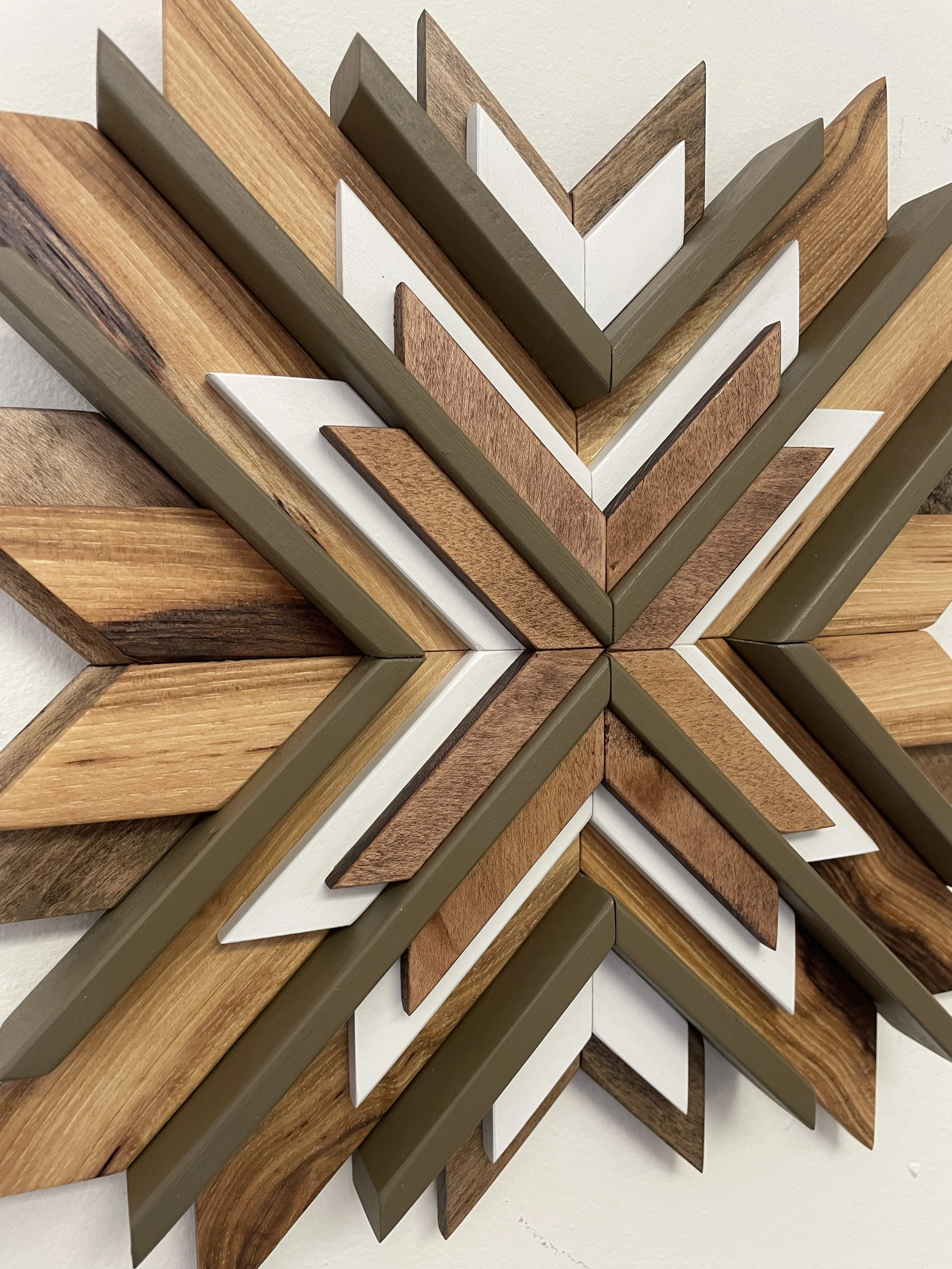 Close up image of a handcrafted sunburst style wooden mosaic in white and green paints with natural and dark stains.