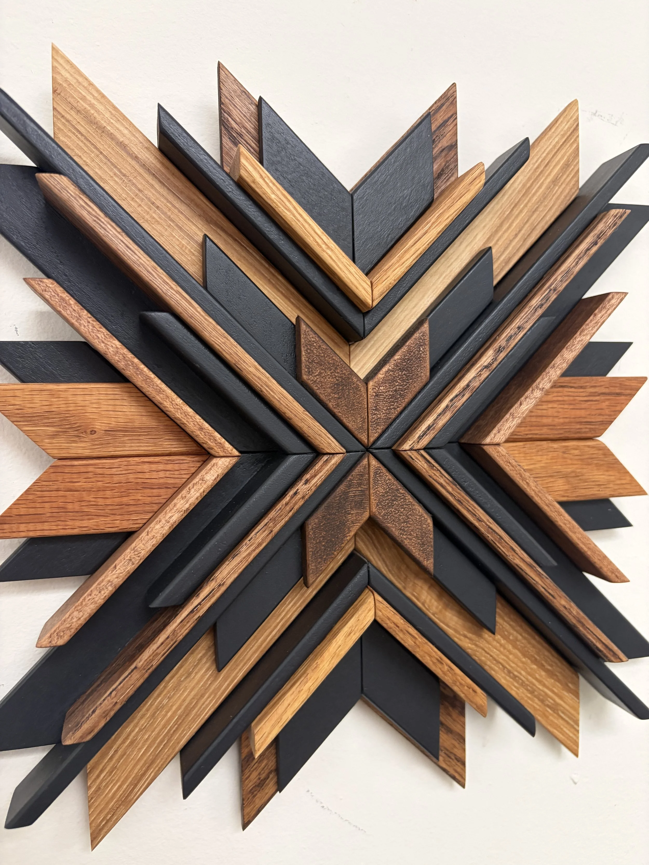Close up view of a wooden sunburst style mosaic in black paint with light and dark stains.