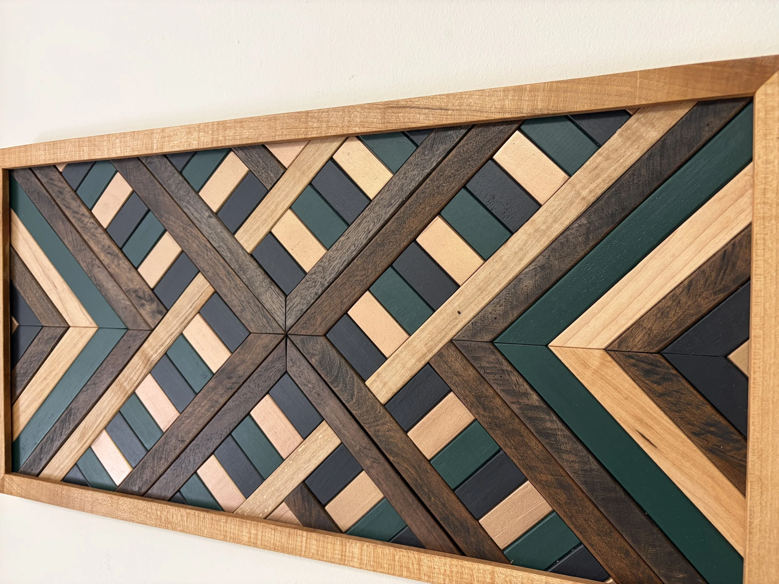 Angled view of a handcrafted framed wooden mosaic in black, green, and gold paint with natural and espresso stains.