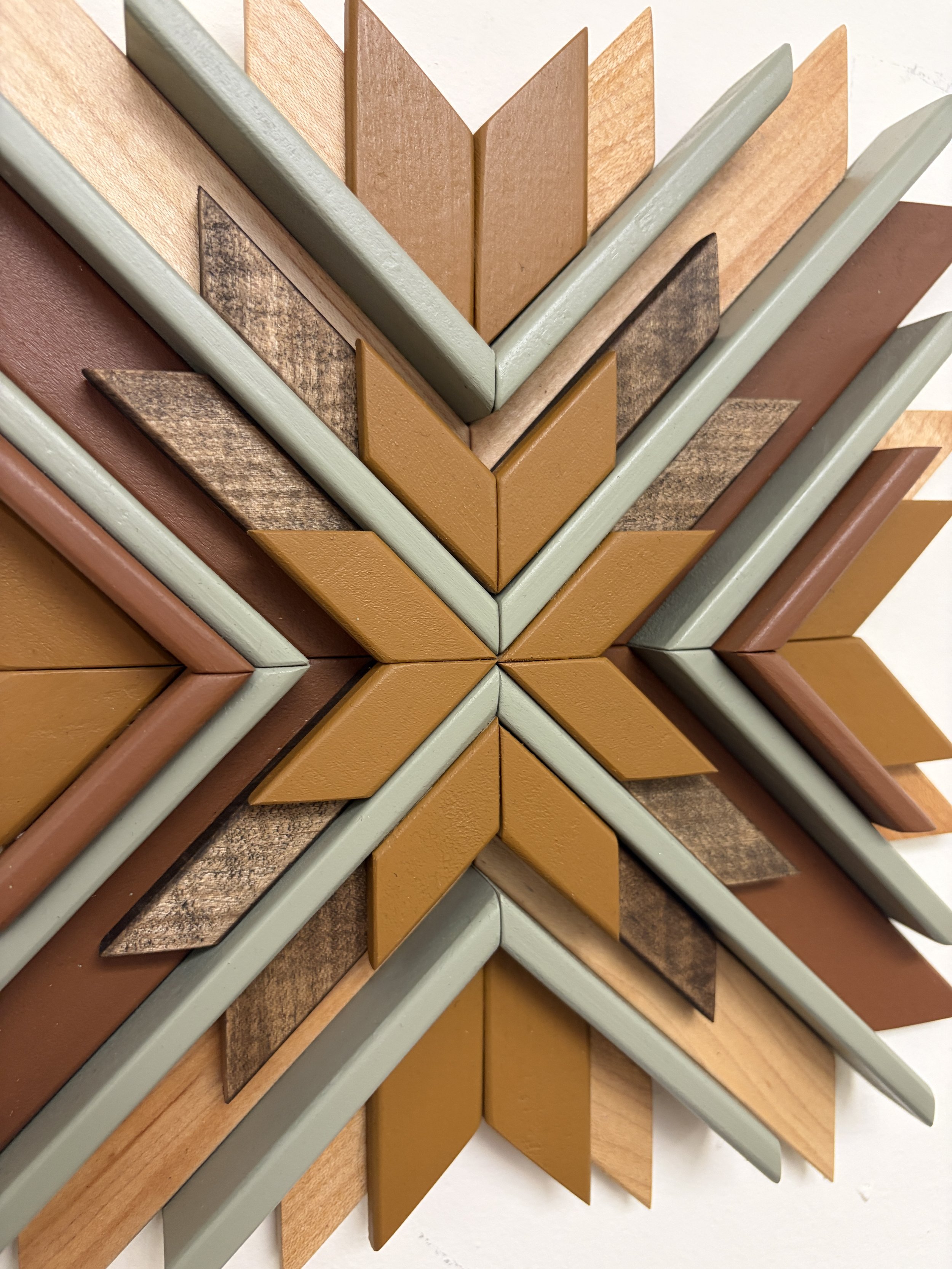 Close up view of a wooden sunburst style mosaic in green, yellow, and orange paint with natural and espresso stains.