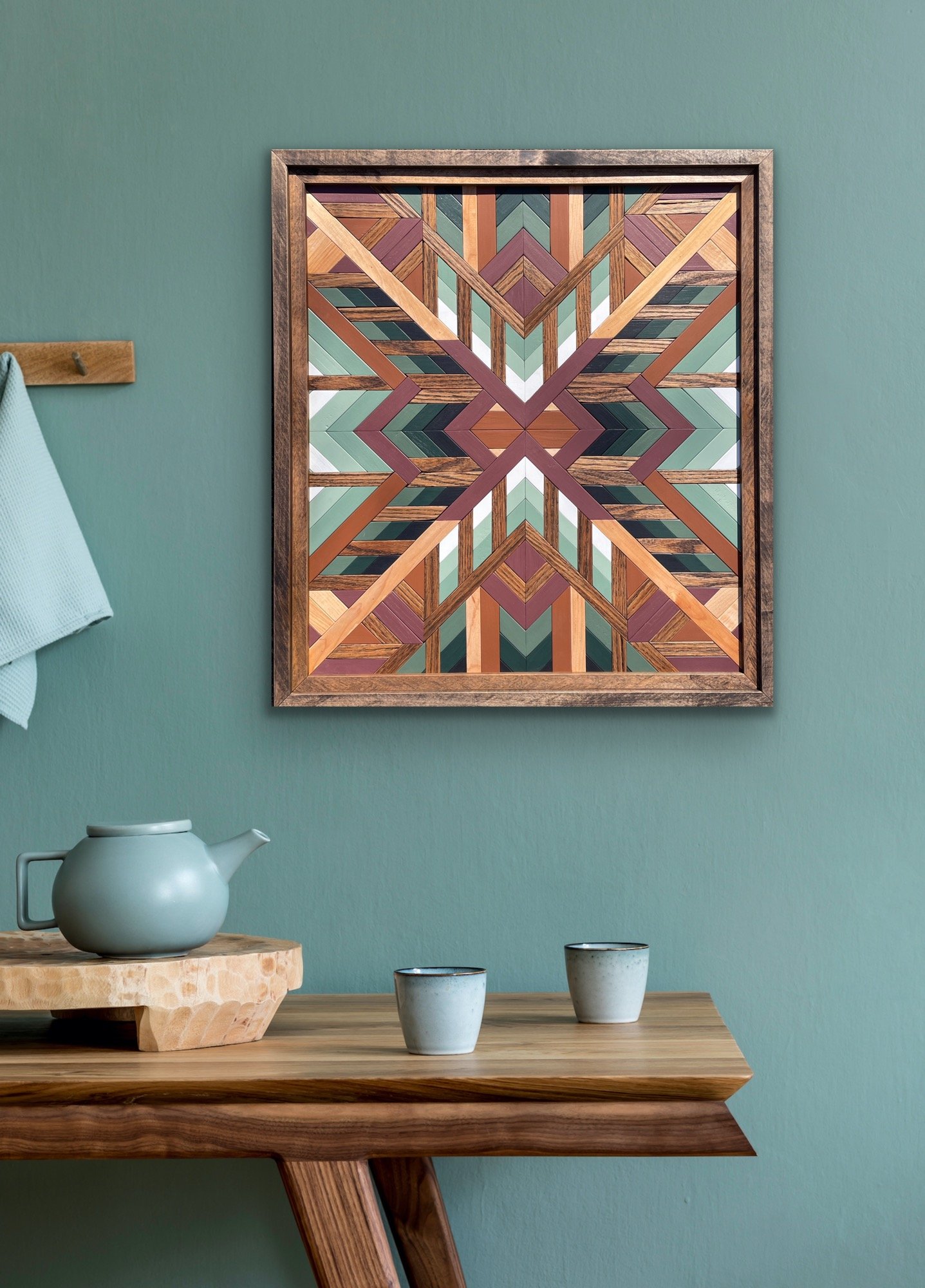 Handcrafted framed wooden mosaic in black, white, pink, orange, and various green paints with natural and espresso stains displayed on a wall.
