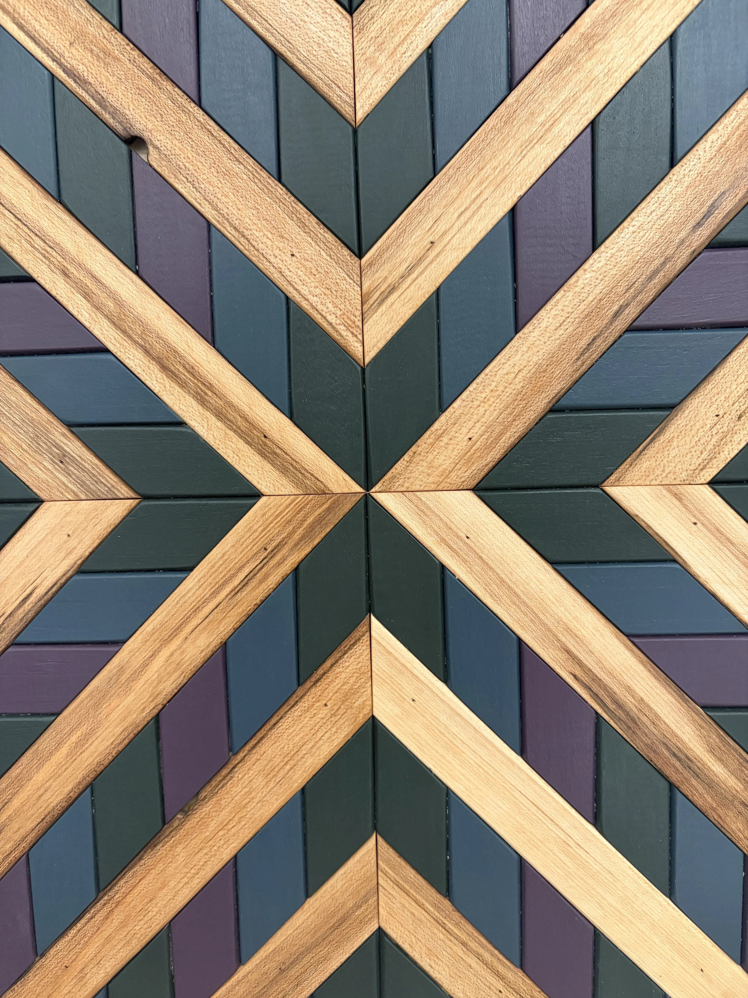 Detailed view of a handcrafted framed wooden mosaic in green, purple, and blue paint with natural stains.