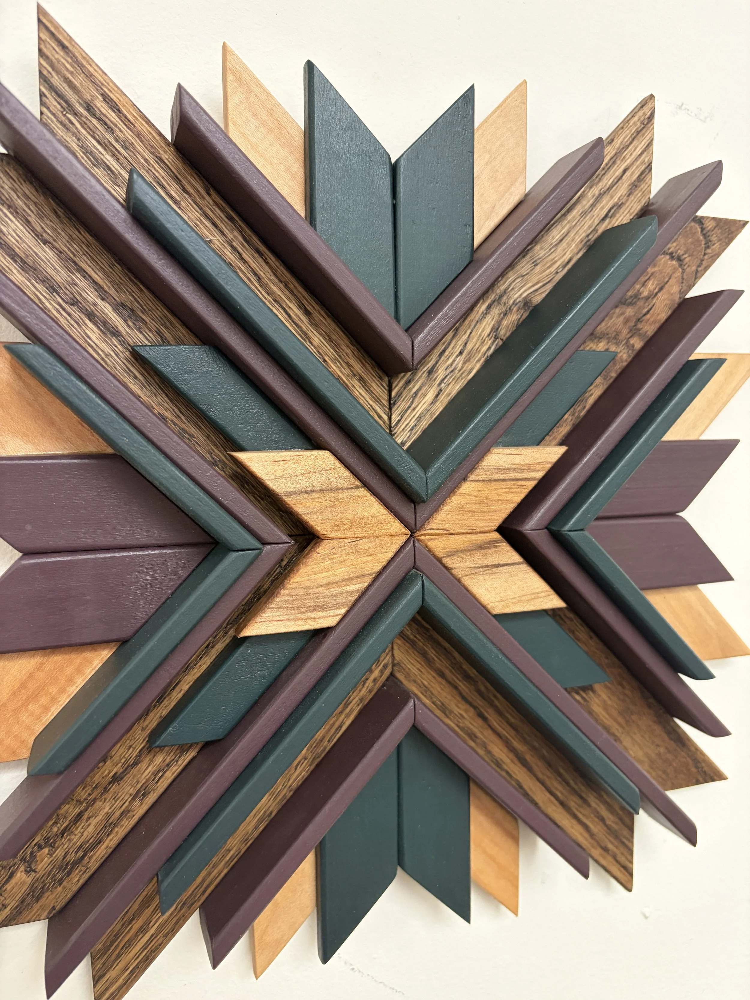 Close up view of a wooden sunburst style mosaic in green and purple paint with natural and espresso stains.